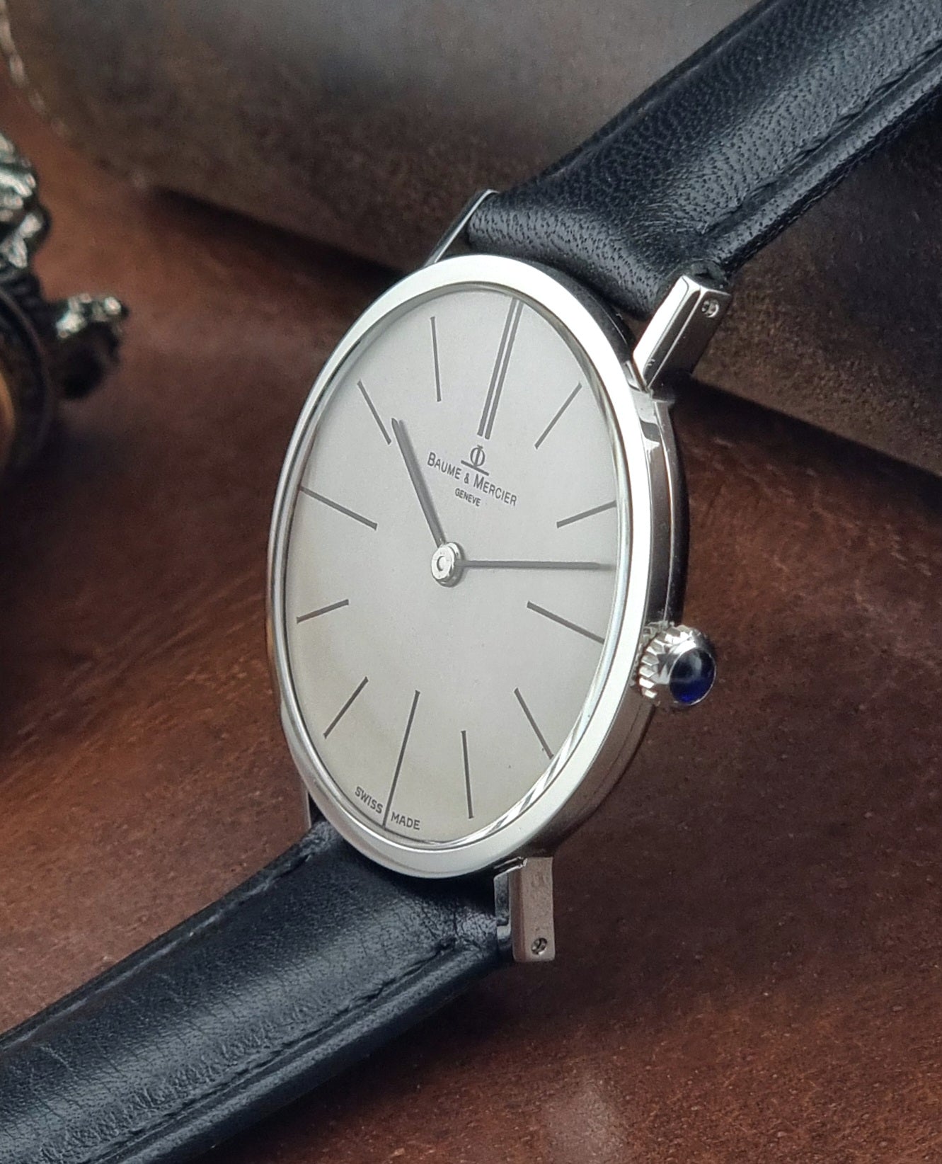Luxury Baume et Mercier watch with a silver case and blue gemstone on a dark leather strap.