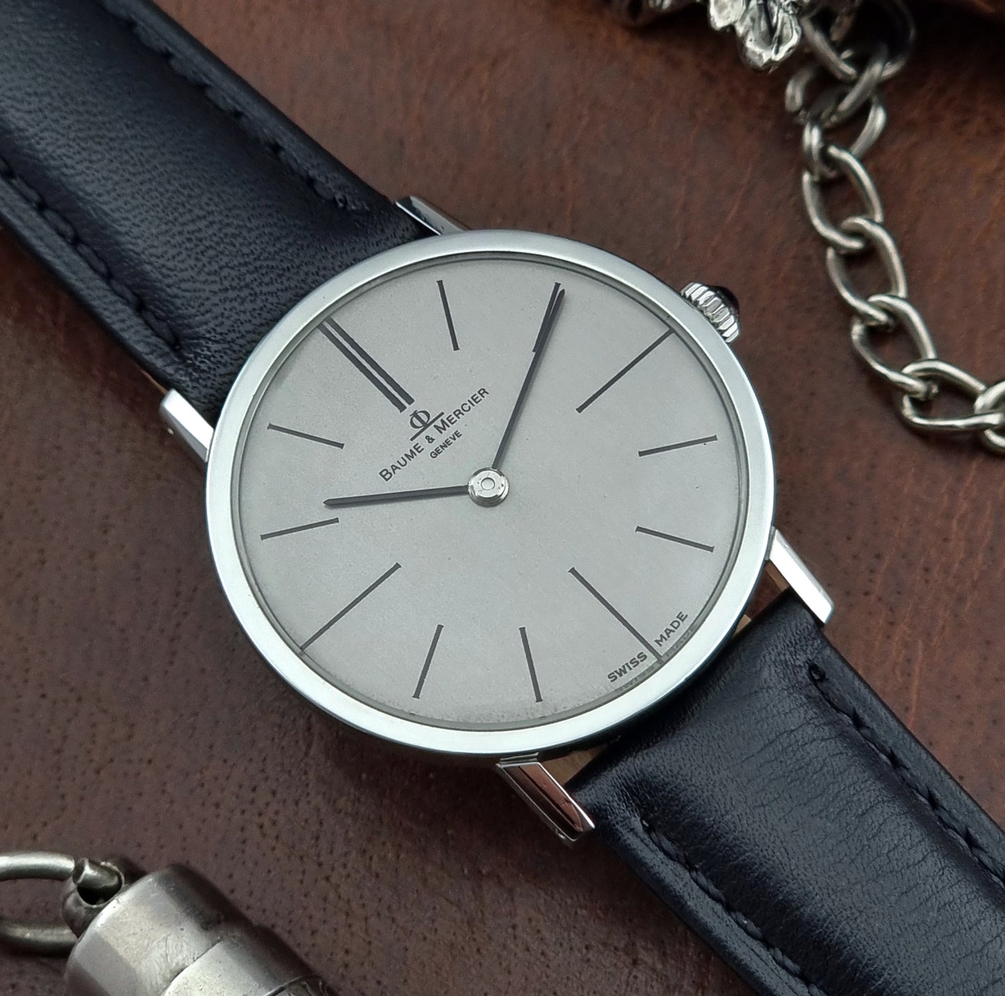 Baume et Mercier Wristwatch with black leather strap and silver case on a brown surface