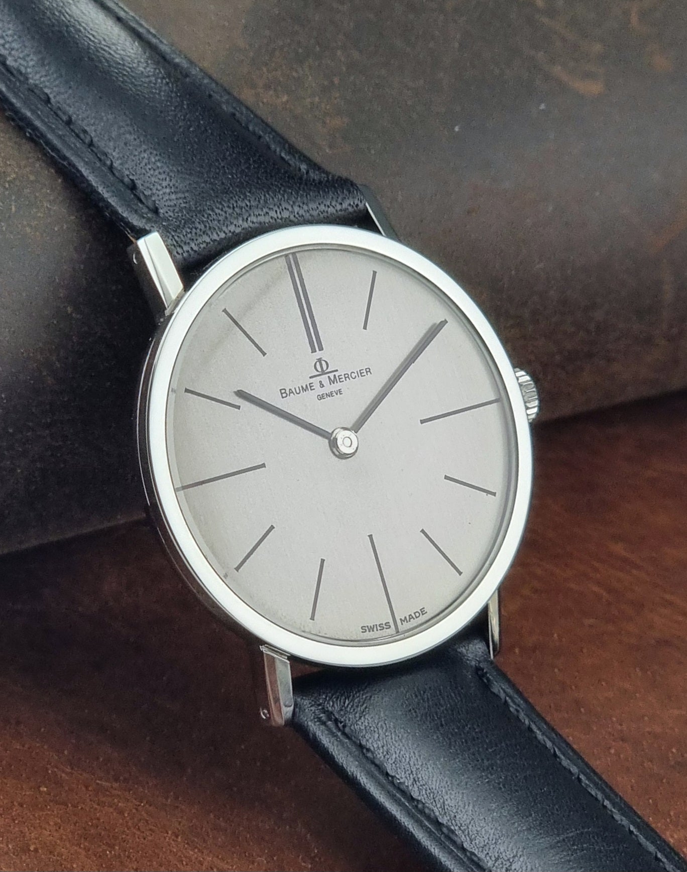 Baume et Mercier Wristwatch with silver dial and black leather strap on a dark background