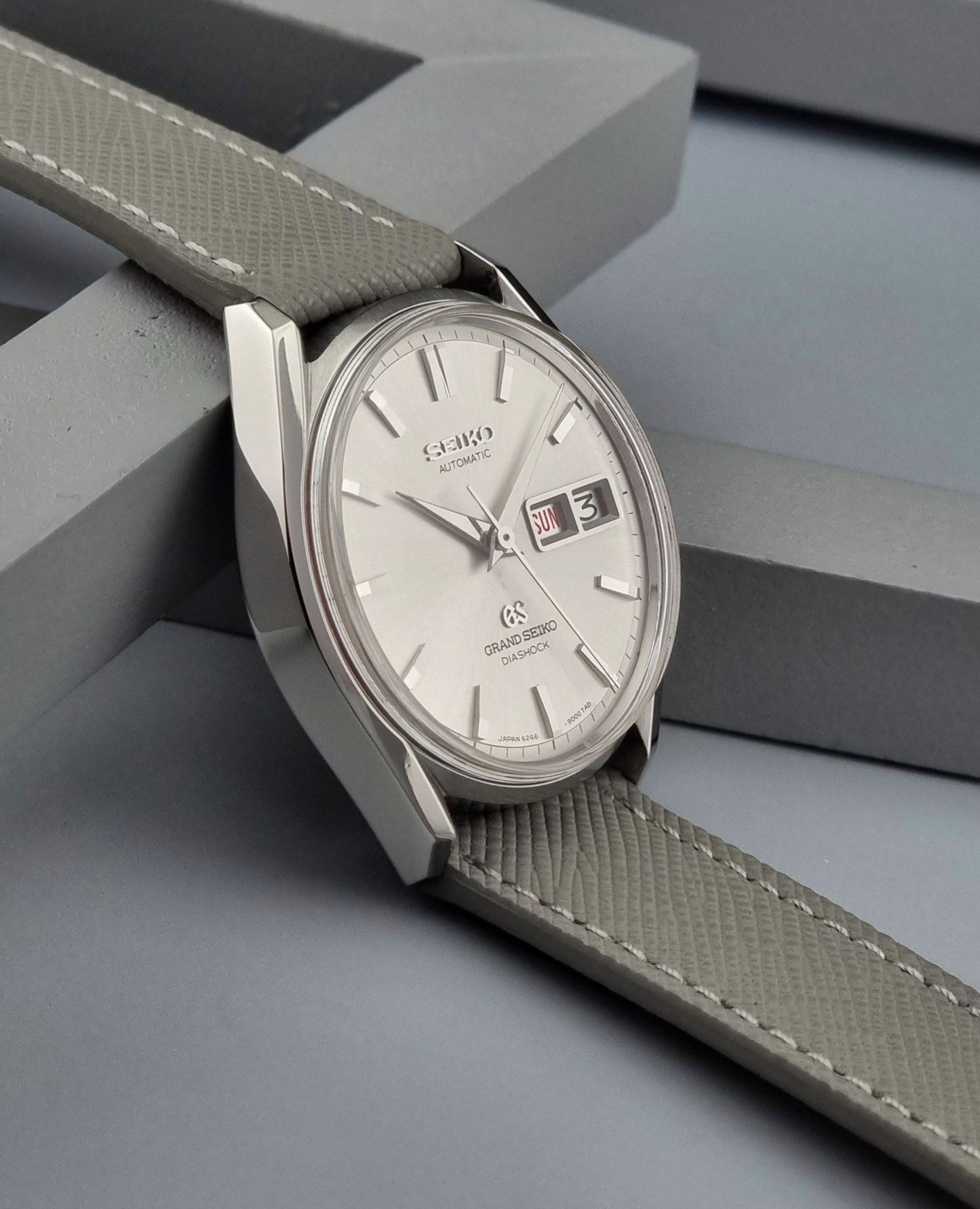 Vintage Grand Seiko Watch with gray strap and silver case on a geometric gray background