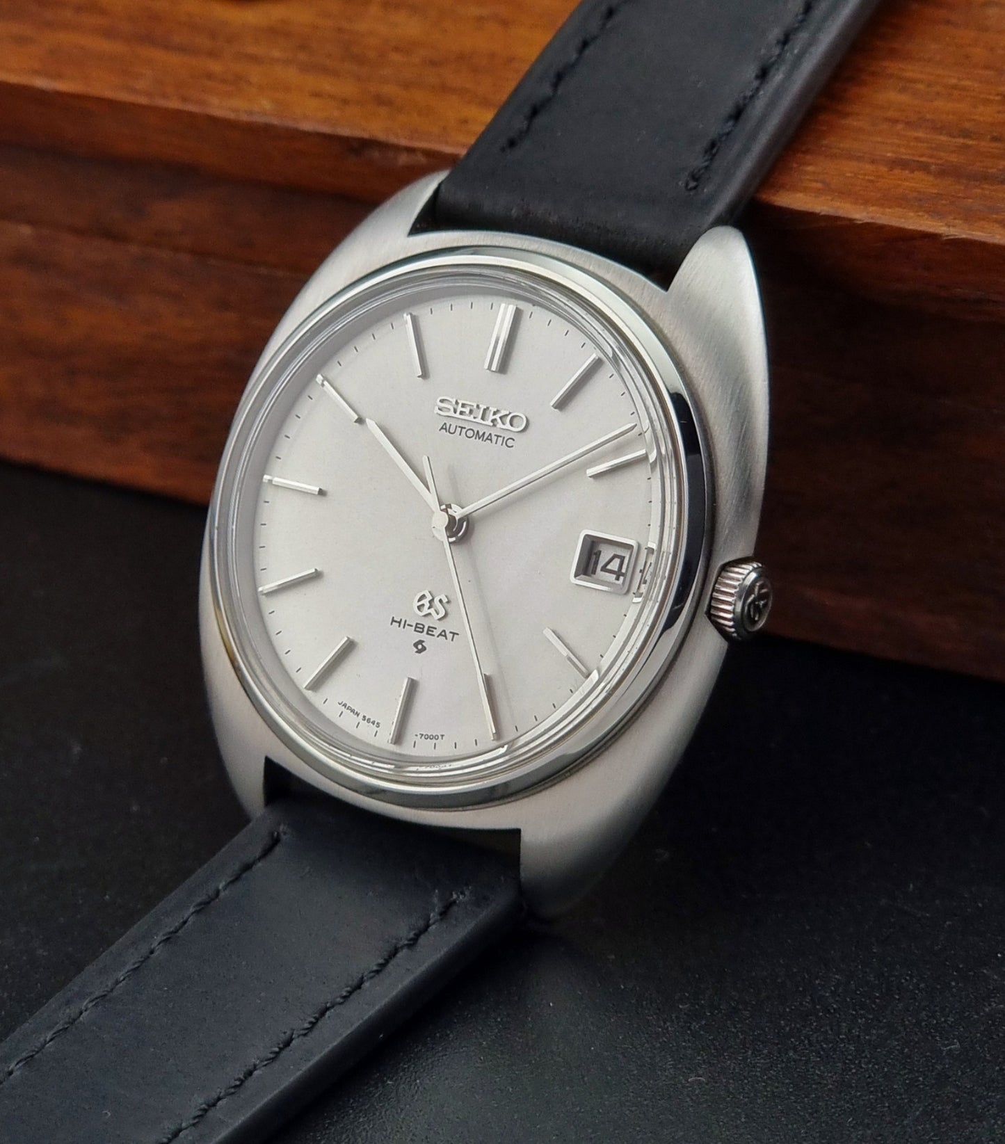 Grand Seiko watch with black leather strap on a wooden surface