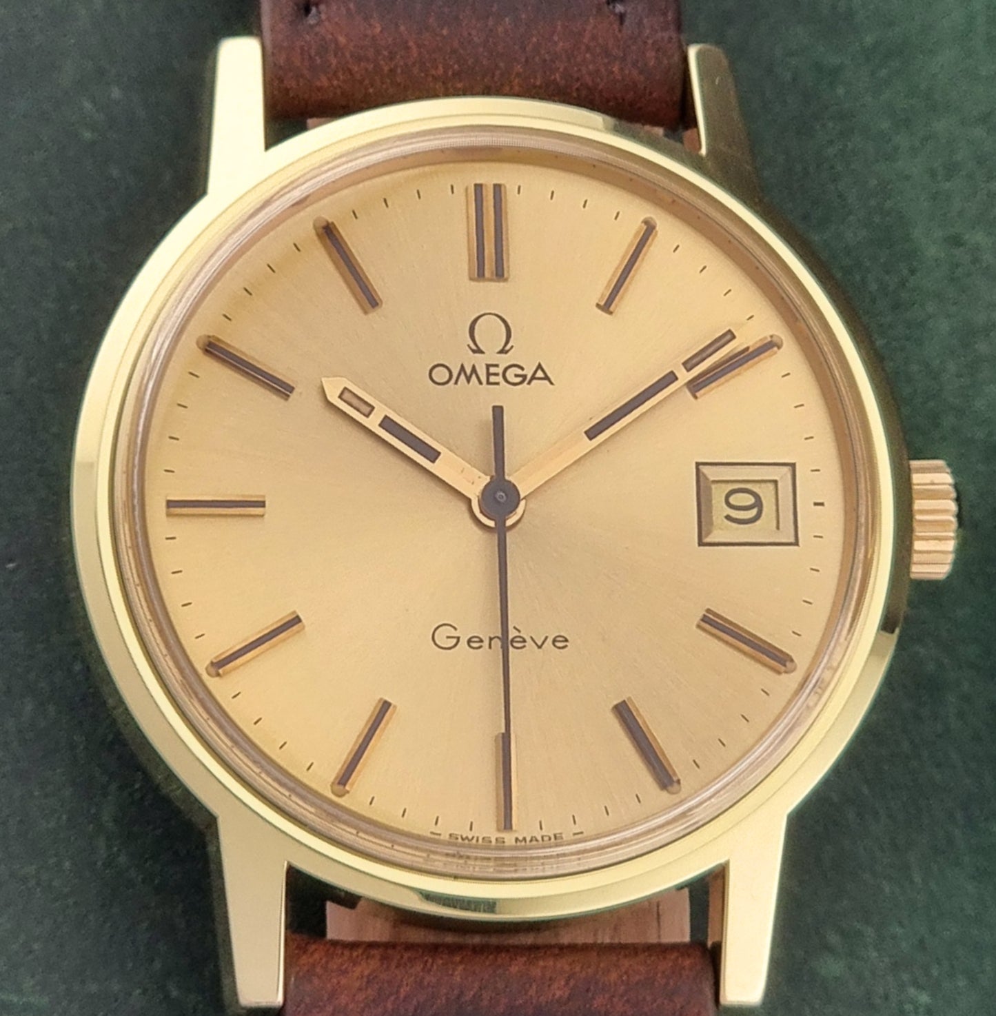 Vintage Gold Omega Geneve watch with brown leather strap on a green background