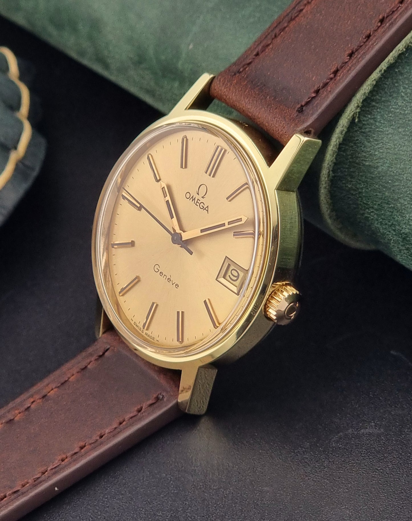 Vintage Gold Omega Geneve watch with brown leather strap on a dark surface