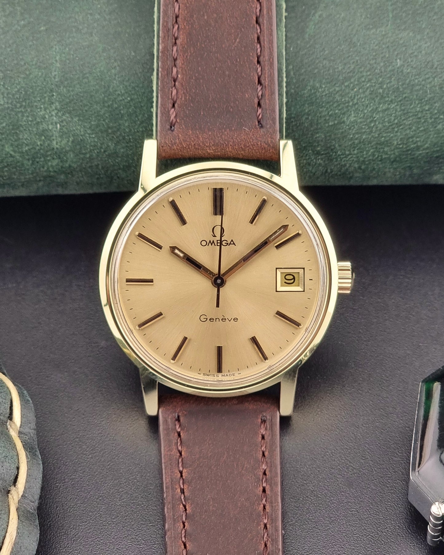 Vintage Gold Omega Geneve watch with brown leather strap on a dark surface