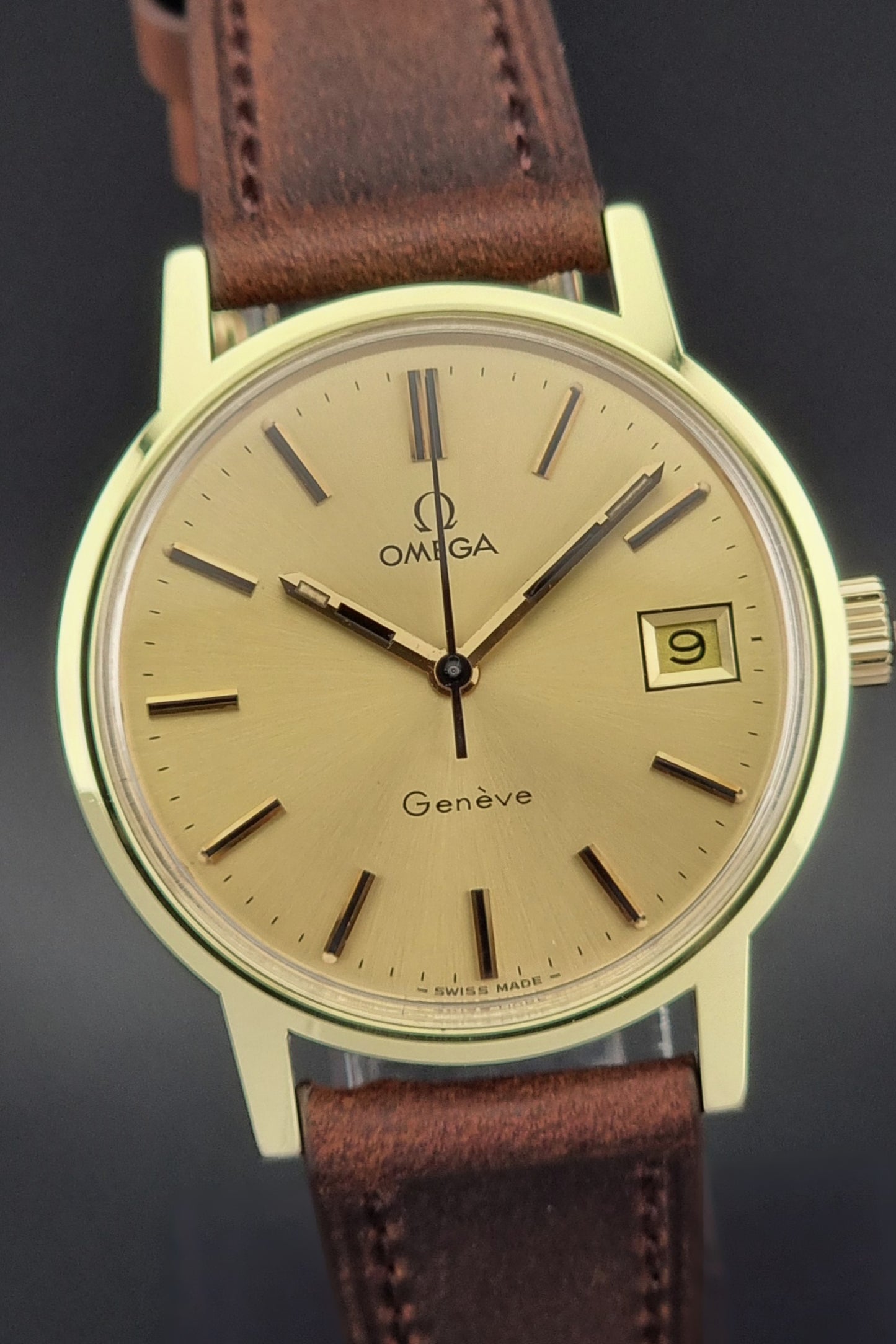 Omega watch with gold face and brown leather strap on a dark background