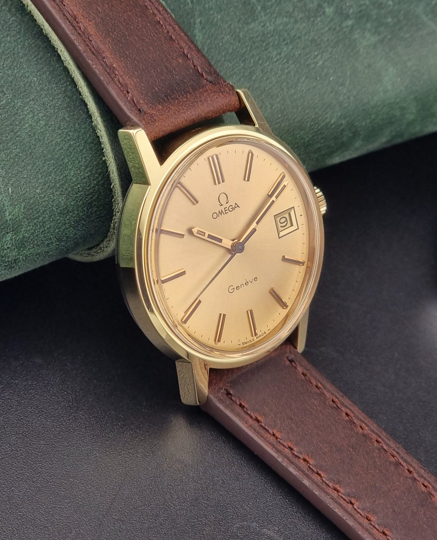 Vintage Gold Omega Geneve watch with brown leather strap on a dark surface