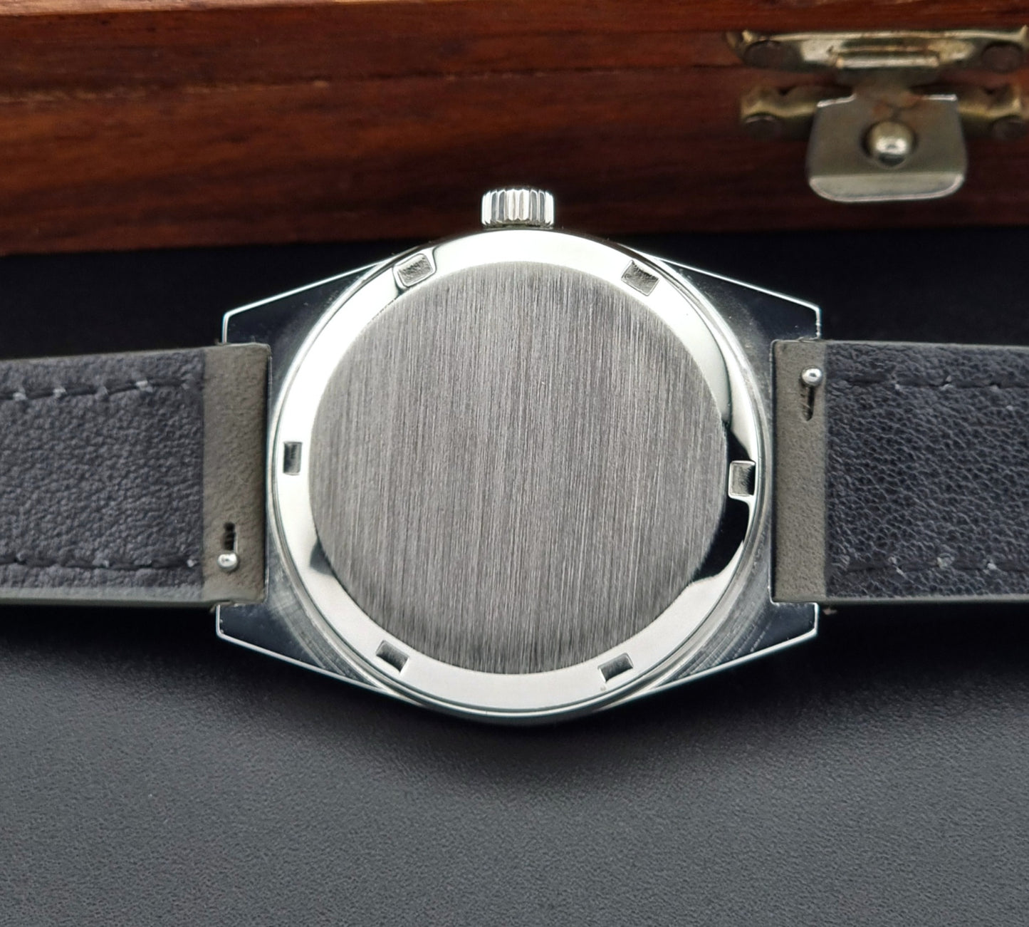 Vintage Omega Geneve case back with black leather strap and metallic case on a dark surface