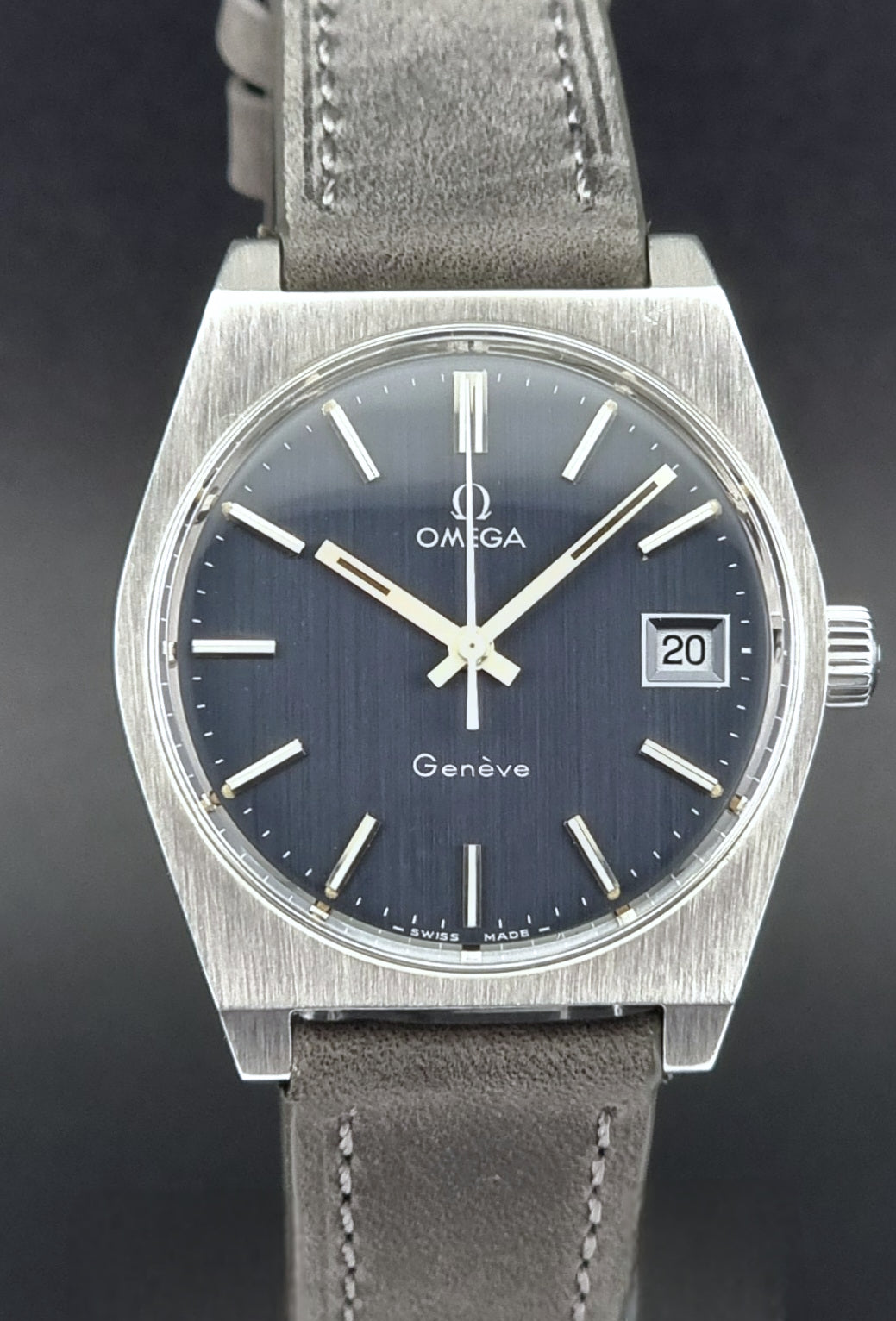 Vintage Omega Geneve watch with dark blue dial and gray leather strap on a black background