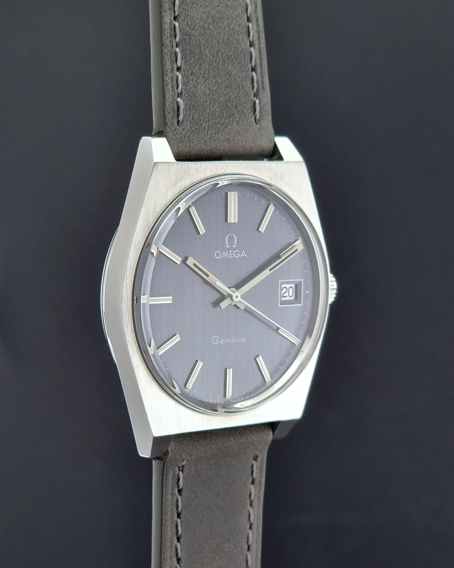 Vintage Omega Geneve watch with gray dial and leather strap on a dark background