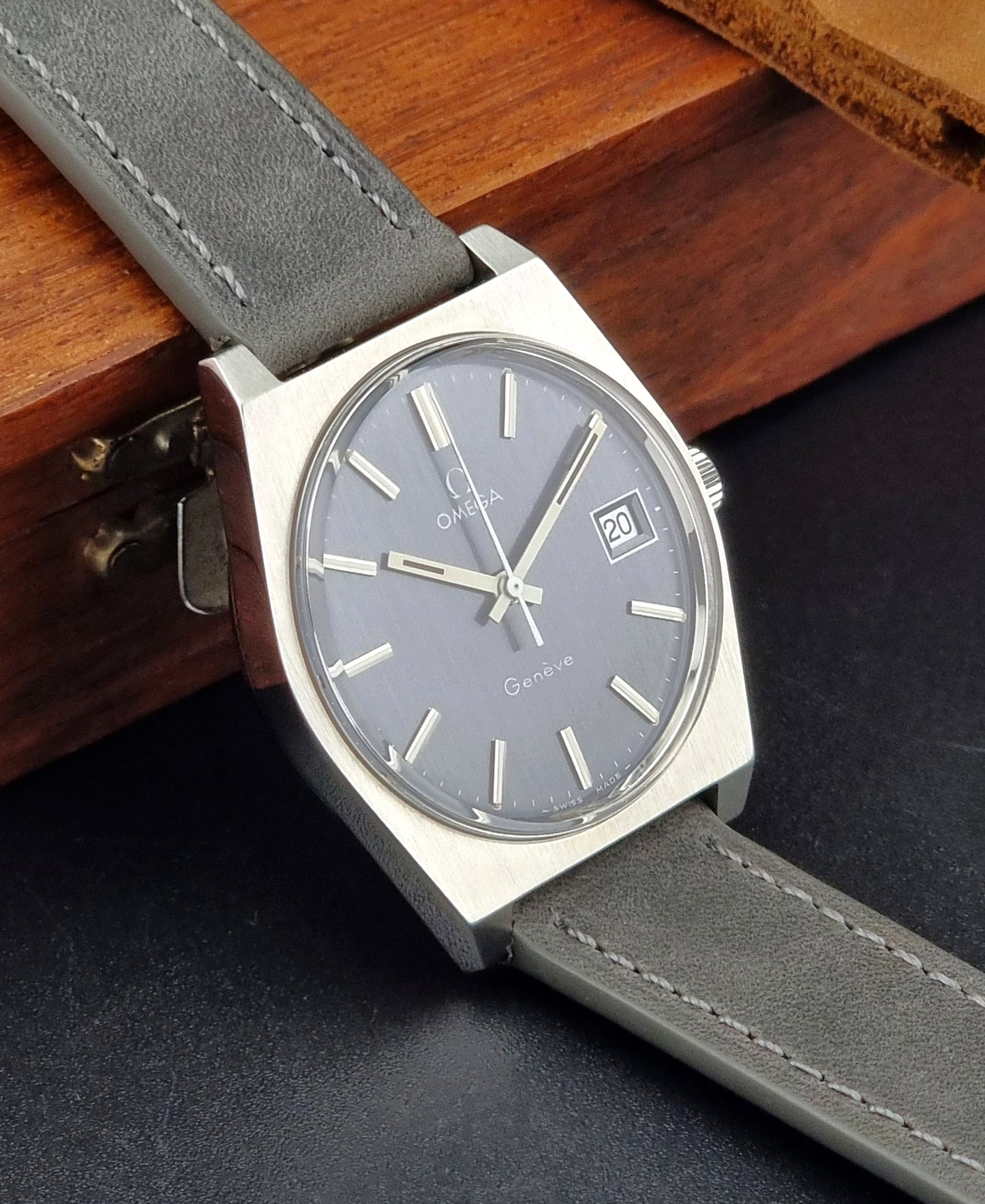 Vintage Omega Geneve Watch with gray strap and dark face on a wooden surface