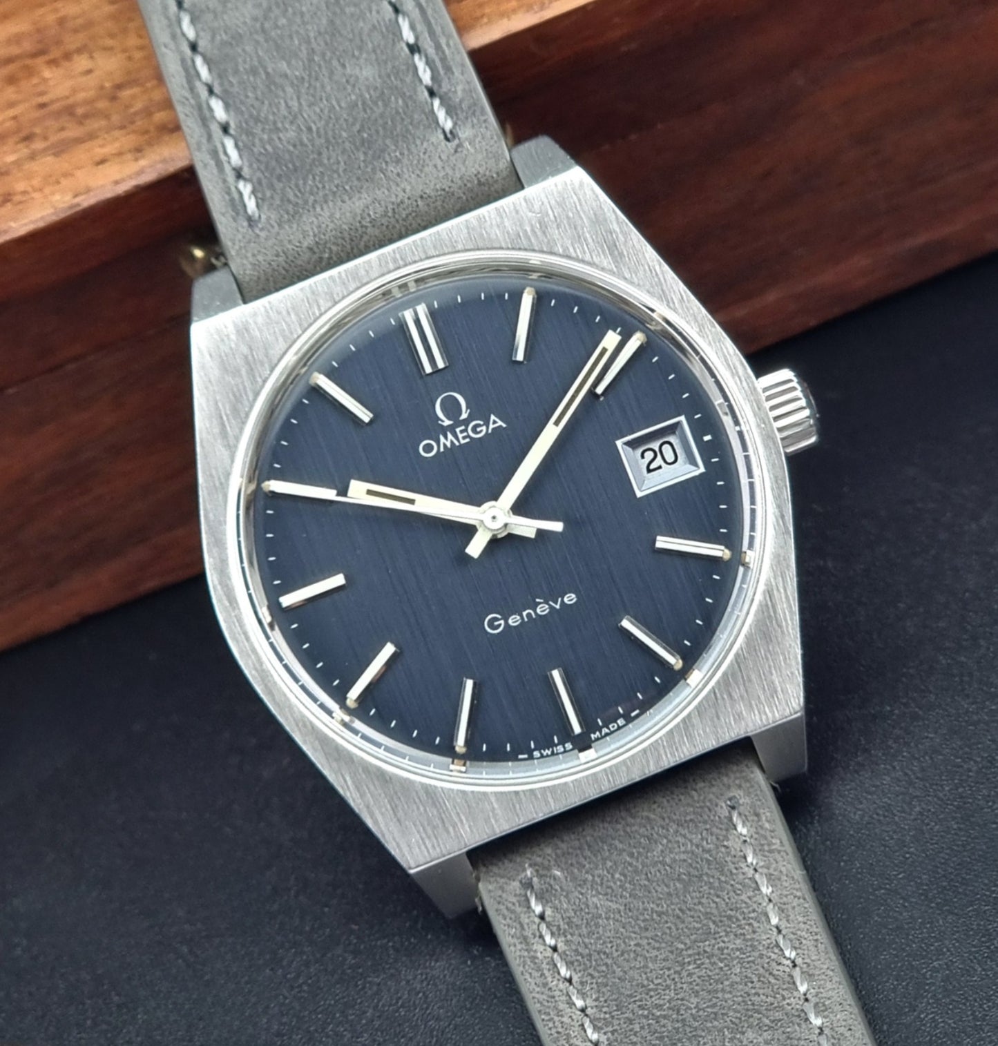 Vintage Omega Geneve watch with blue dial and gray leather strap on a dark surface