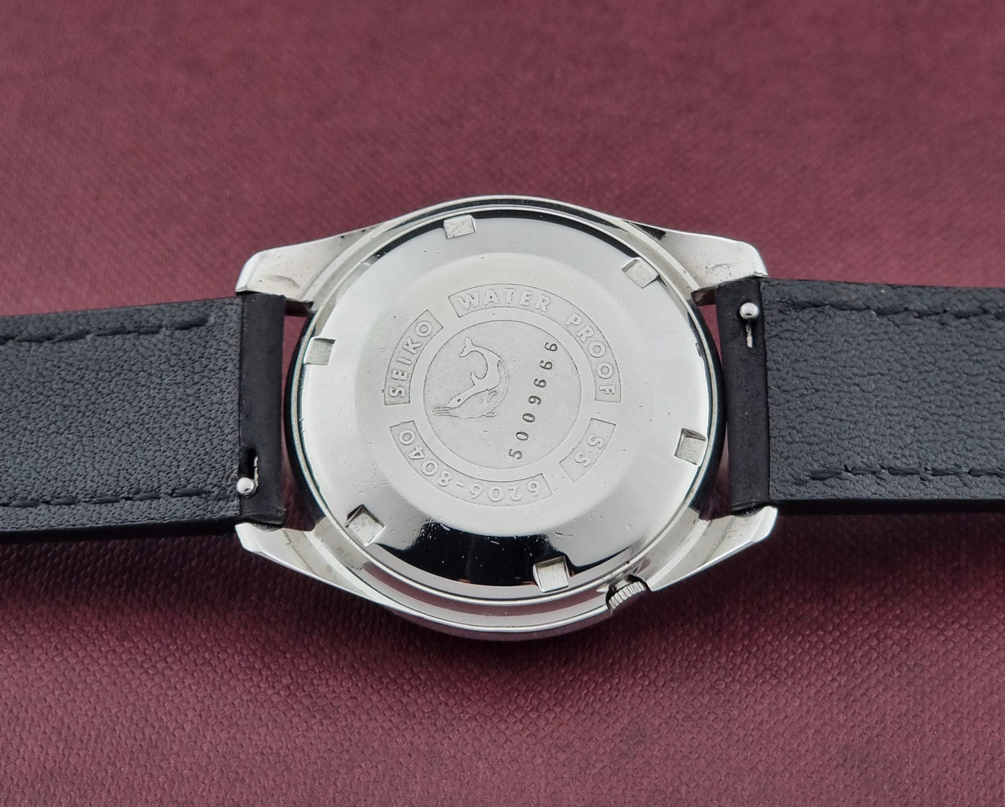 Seiko Seikomatic 6206-8040 Wristwatch case back view on a black leather strap on a maroon background