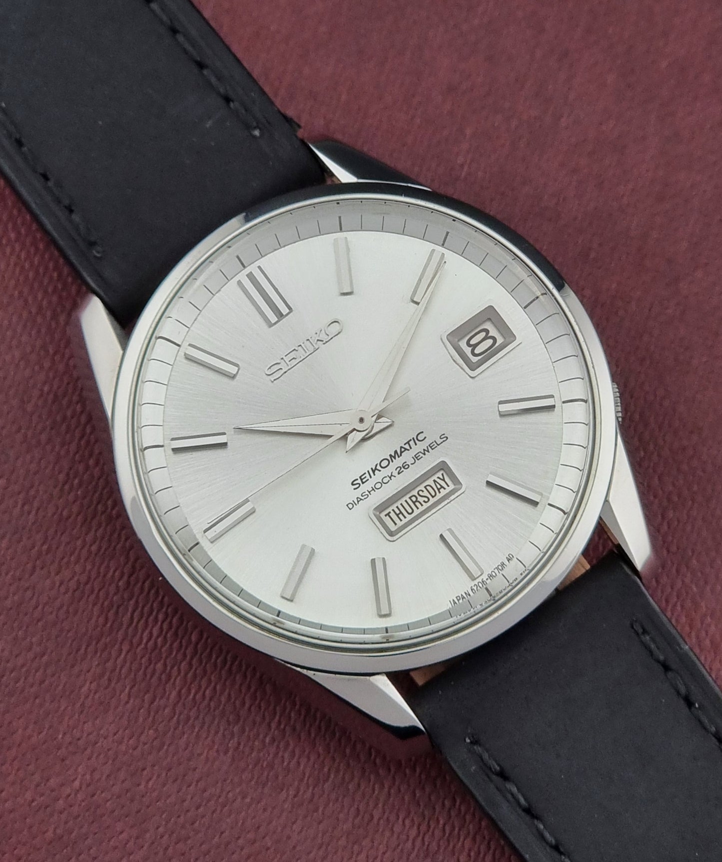 Seiko Seikomatic 6206-8040 Wristwatch with black leather strap on a maroon background