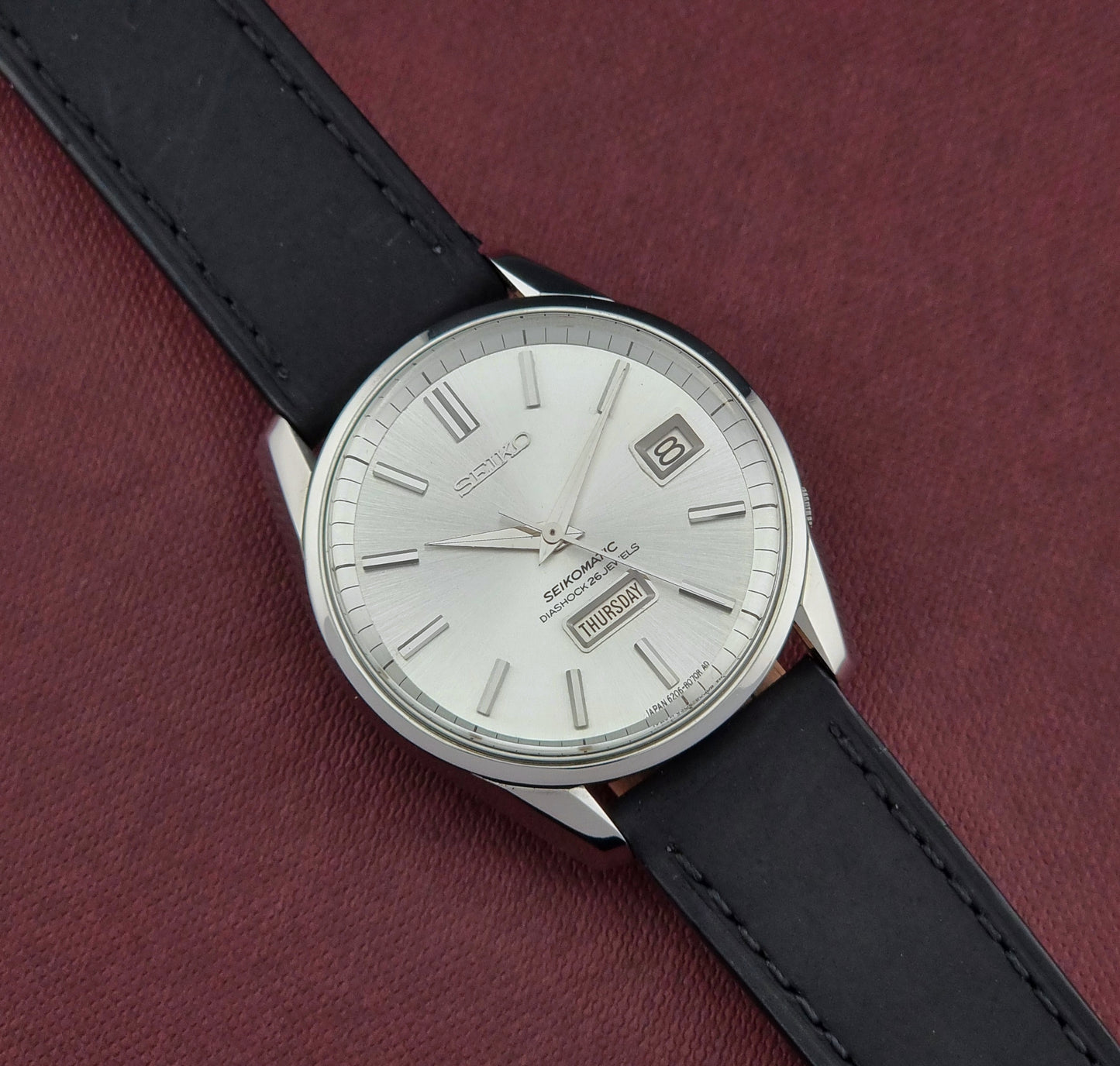 Seiko Seikomatic 6206-8040 Wristwatch with black leather strap and silver case on a maroon background
