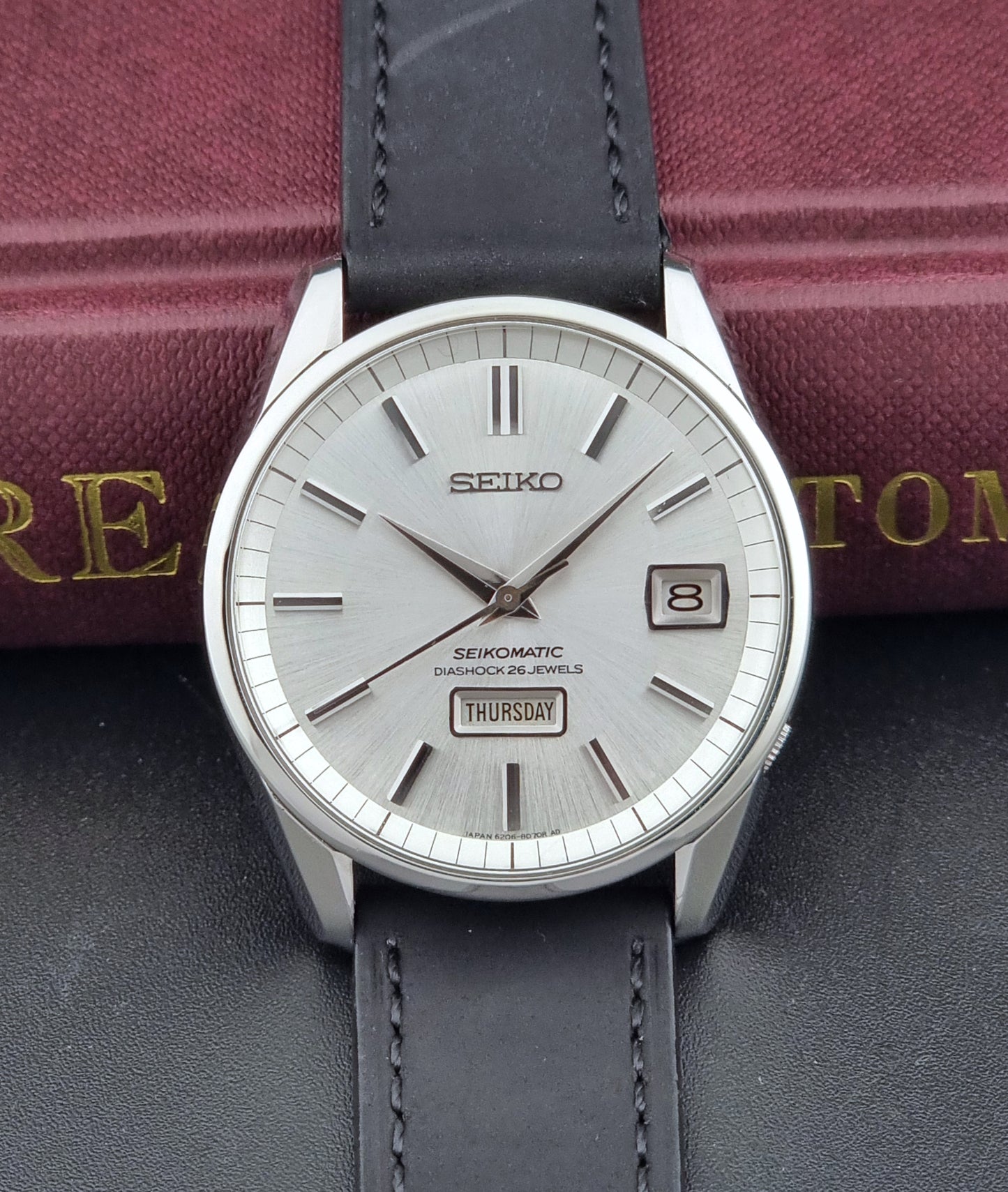 Seiko Seikomatic 6206-8040 Wristwatch with a silver dial and black leather strap on a dark surface.