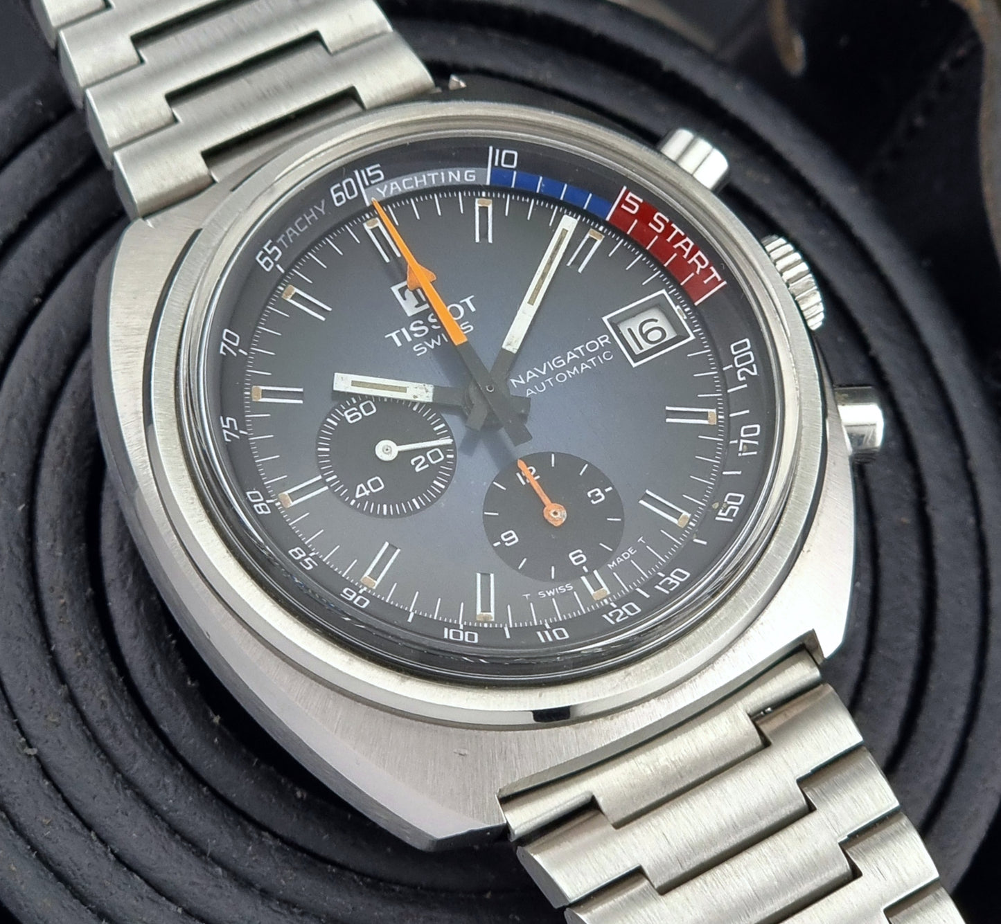 Close-up of a Tissot watch with a silver bracelet on a textured black background