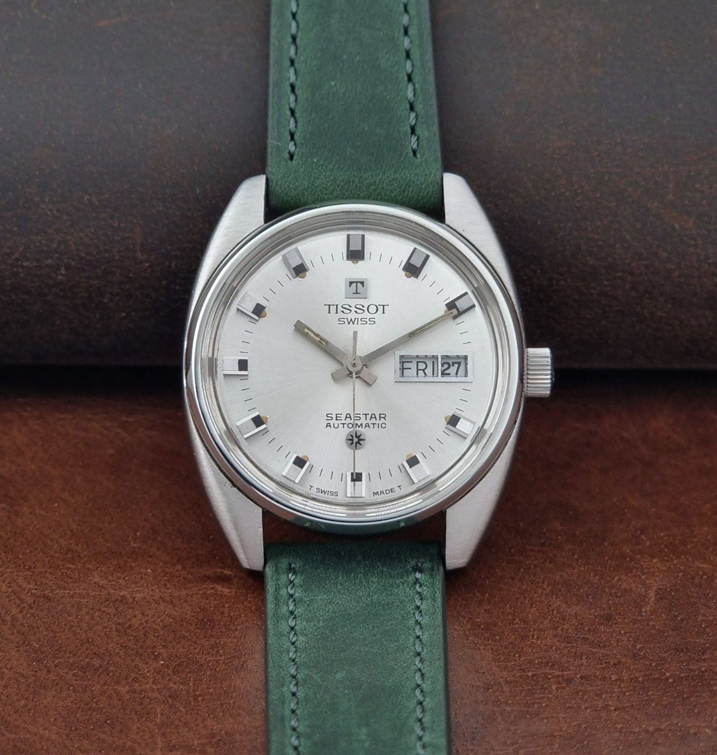 Tissot Seastar 46660 watch with green leather strap on a brown surface