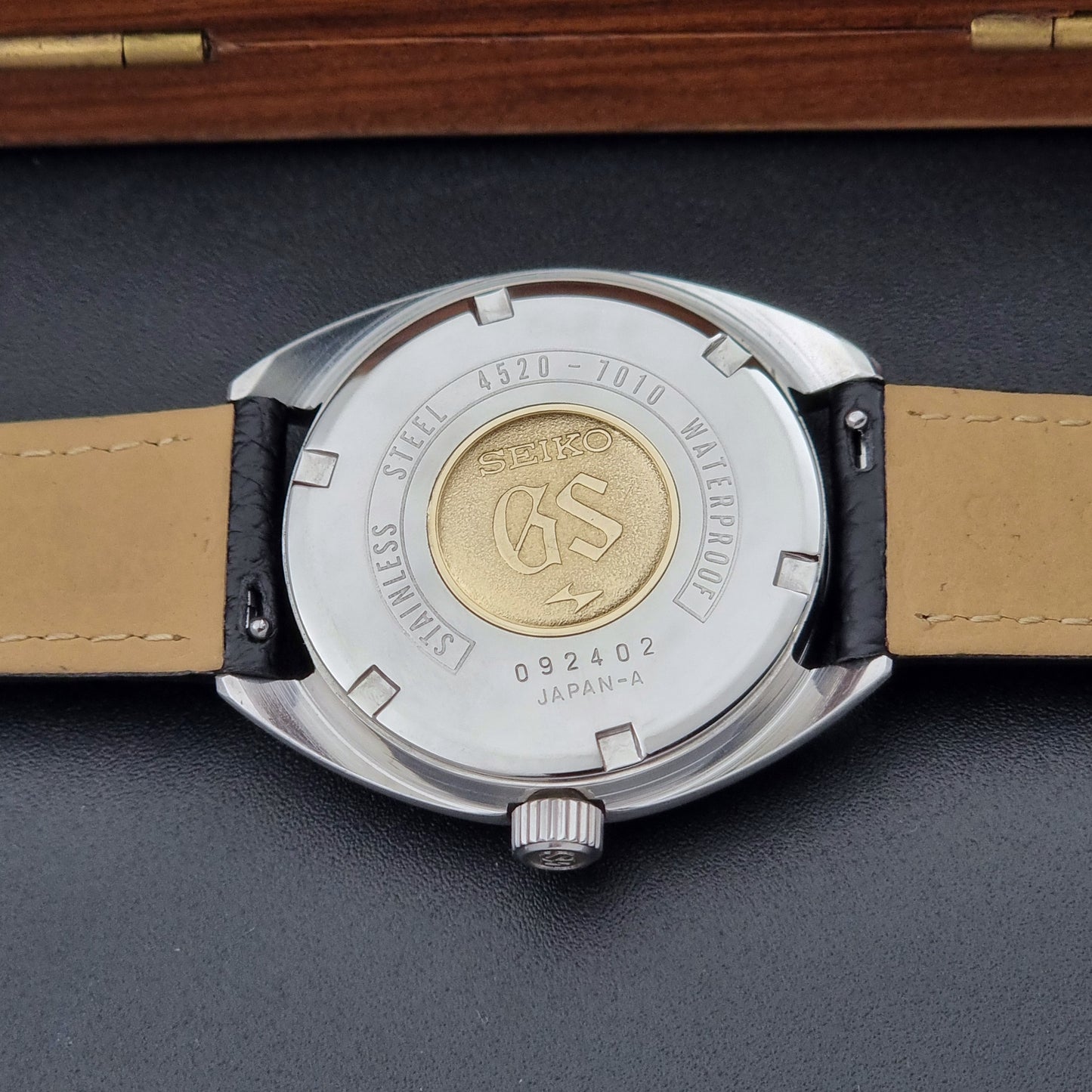 Grand Seiko watch 4520-7010 close up of its case back showing the GS gold medallion with black leather strap on a on a dark surface