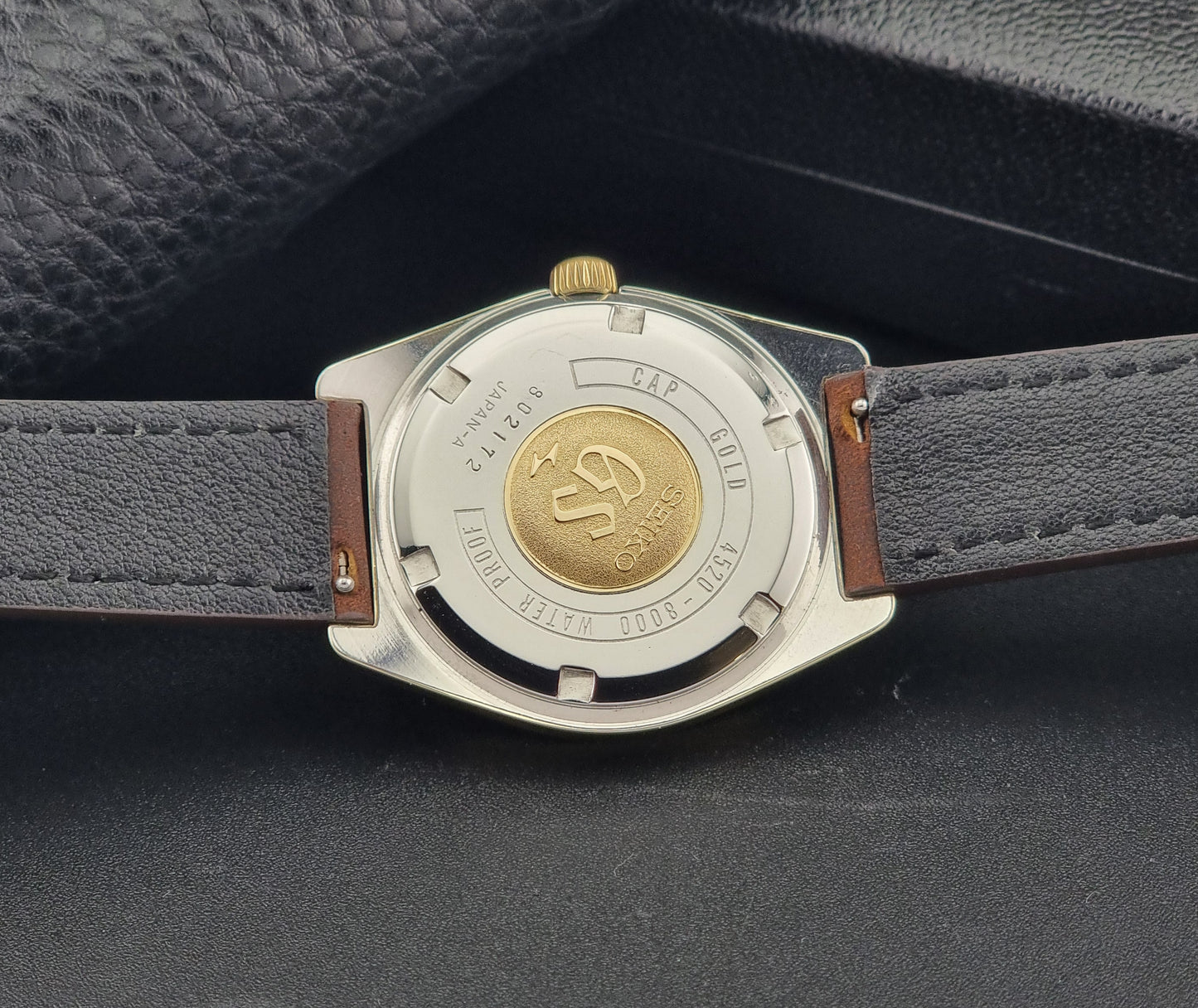 Vintage Grand Seiko Gold 4520-8000 wristwatch with a brown leather strap on a dark textured background case back