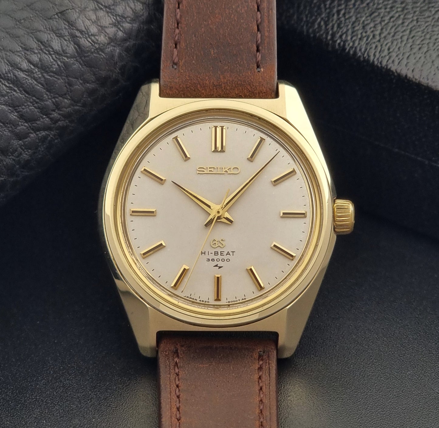 Vintage Grand Seiko Gold 4520-8000 wristwatch with a brown leather strap on a dark textured background close up front view