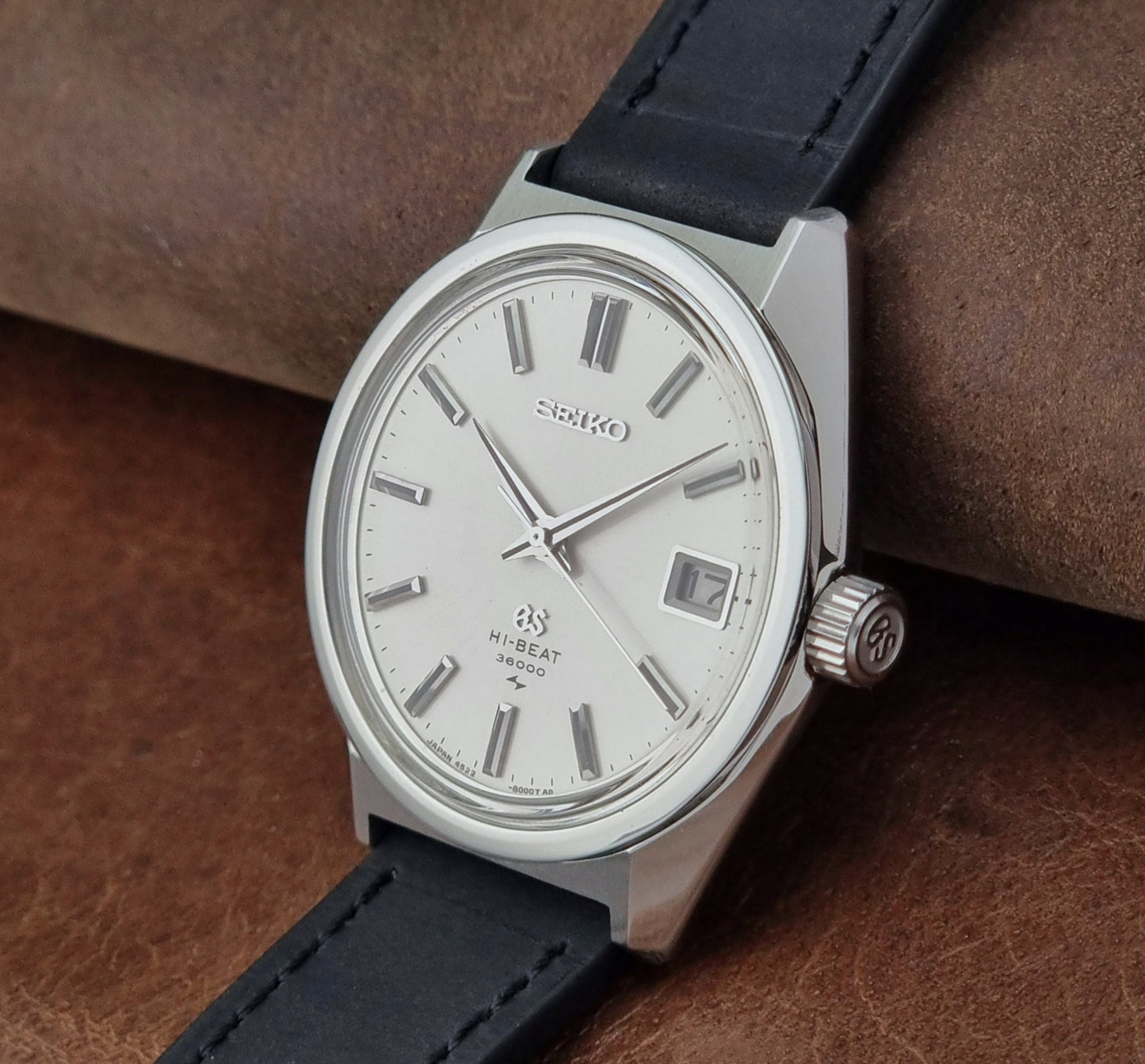 Vintage Grand Seiko 4522-8000 watch with black strap on a brown leather surface