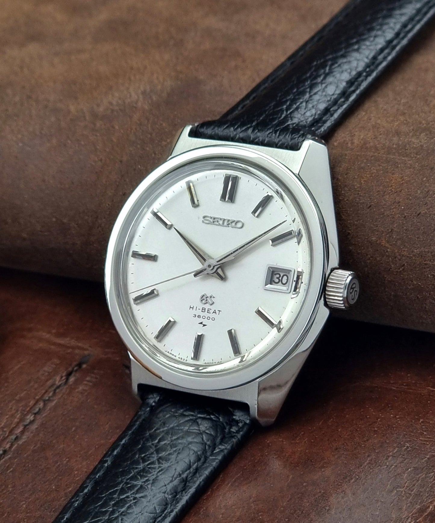 Vintage Grand Seiko watch with black leather strap on a brown textured background