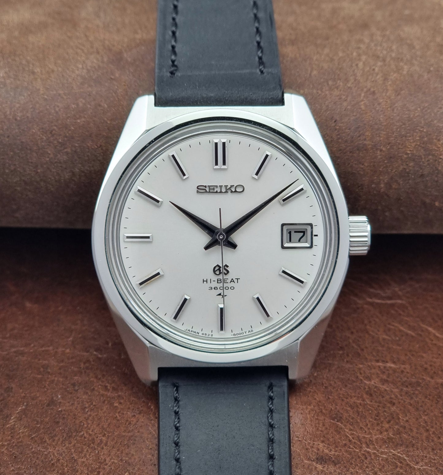 Vintage Grand Seiko 4522-8000 watch with black leather strap on a brown leather surface