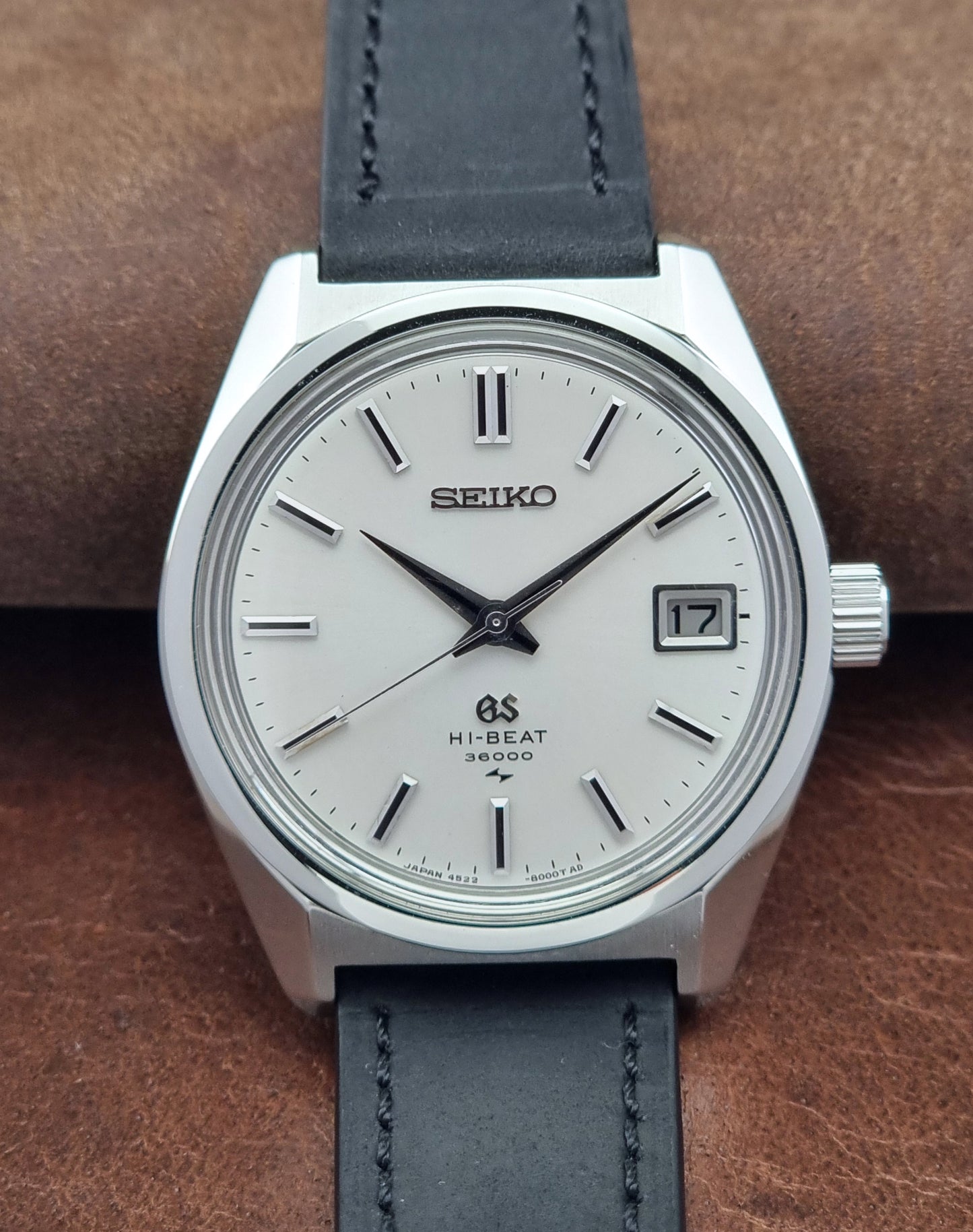 Vintage Grand Seiko 4522-8000 watch with a silver case and black leather strap on a brown background