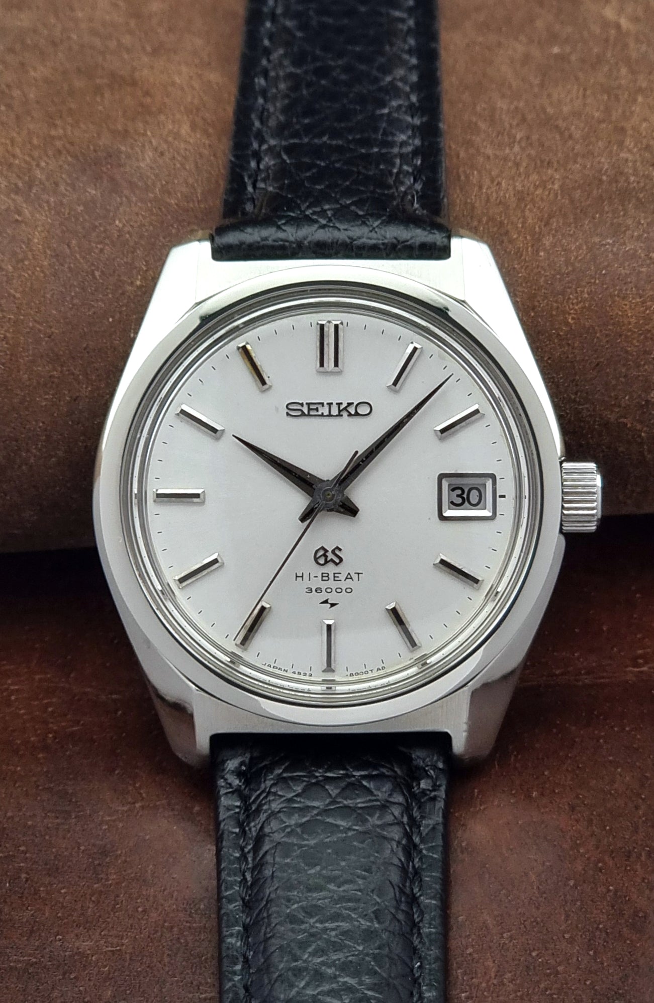 Vintage Grand Seiko watch with black leather strap on a brown background