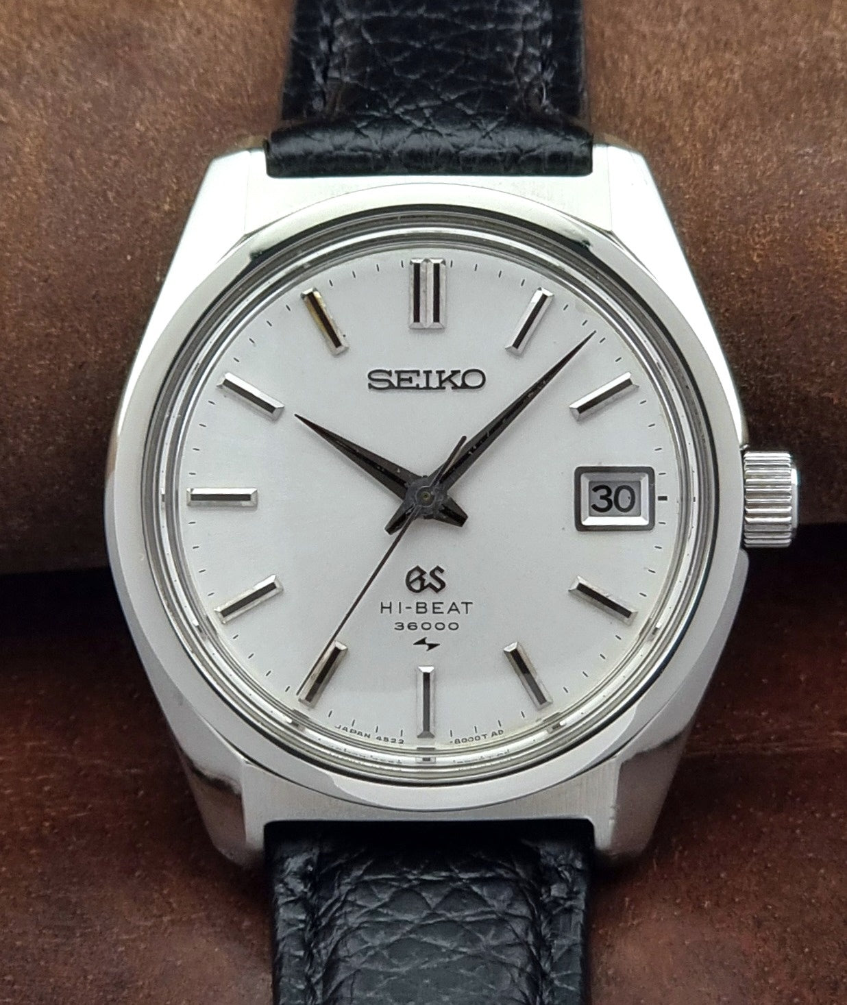 Vintage Grand Seiko watch with black leather strap on a brown background