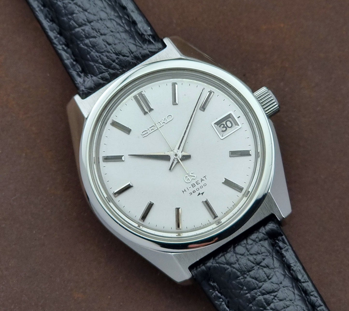 Vintage Grand Seiko watch with black leather strap on a brown background