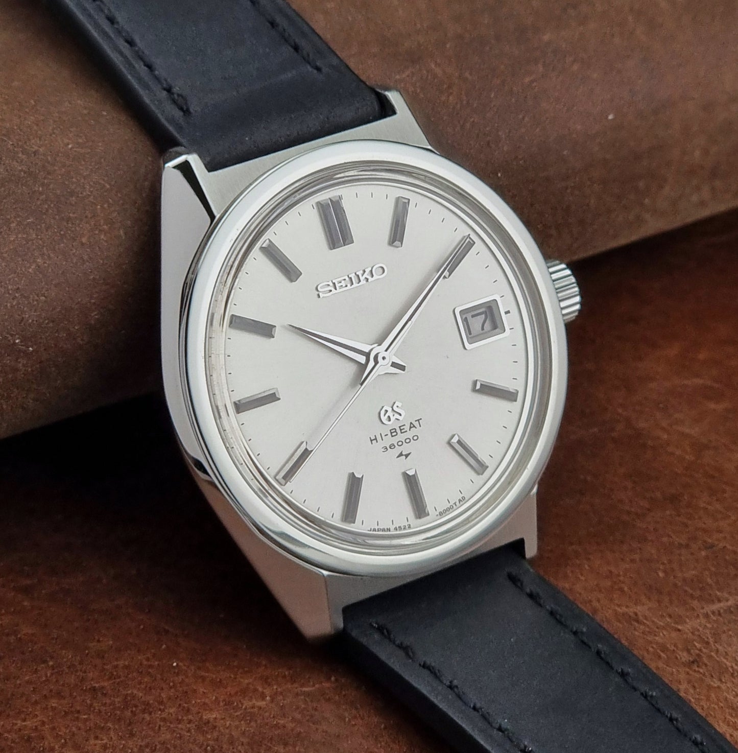 Vintage Grand Seiko 4522-8000 watch with black leather strap on a brown textured background