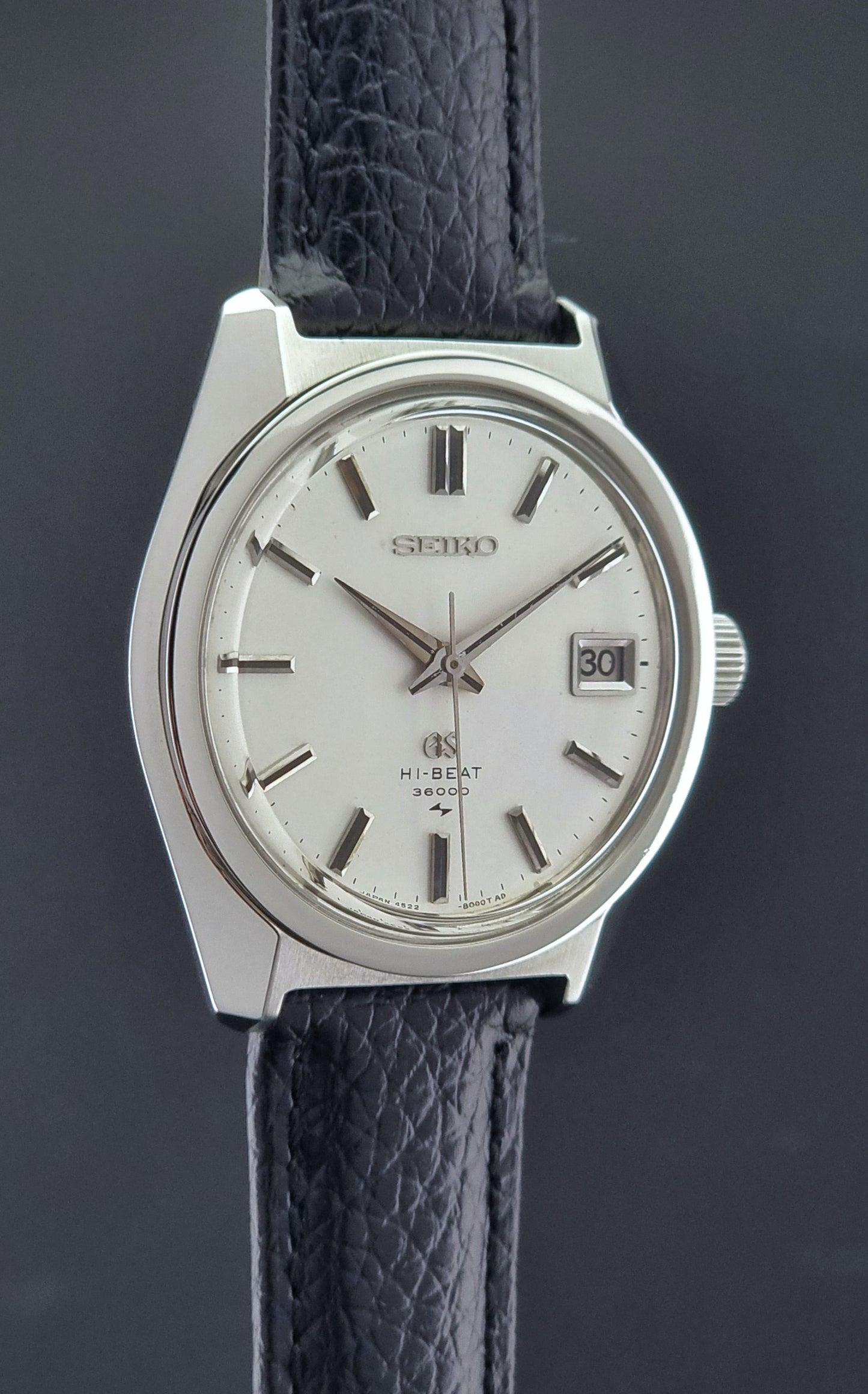 Vintage Grand Seiko watch with a silver case and black leather strap on a dark background