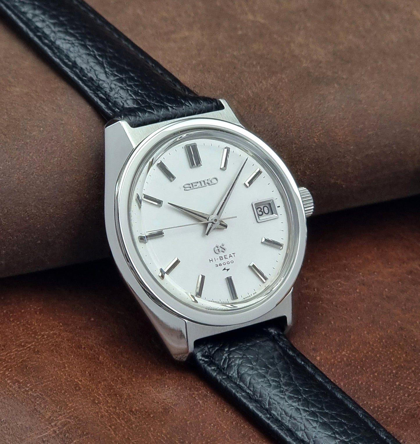 Vintage Grand Seiko watch with black leather strap on a brown leather surface