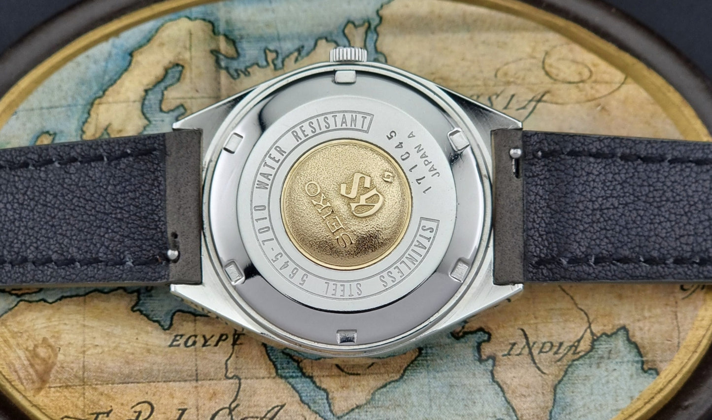 Vintage Grand Seiko Watch case back with a gold emblem on a world map background