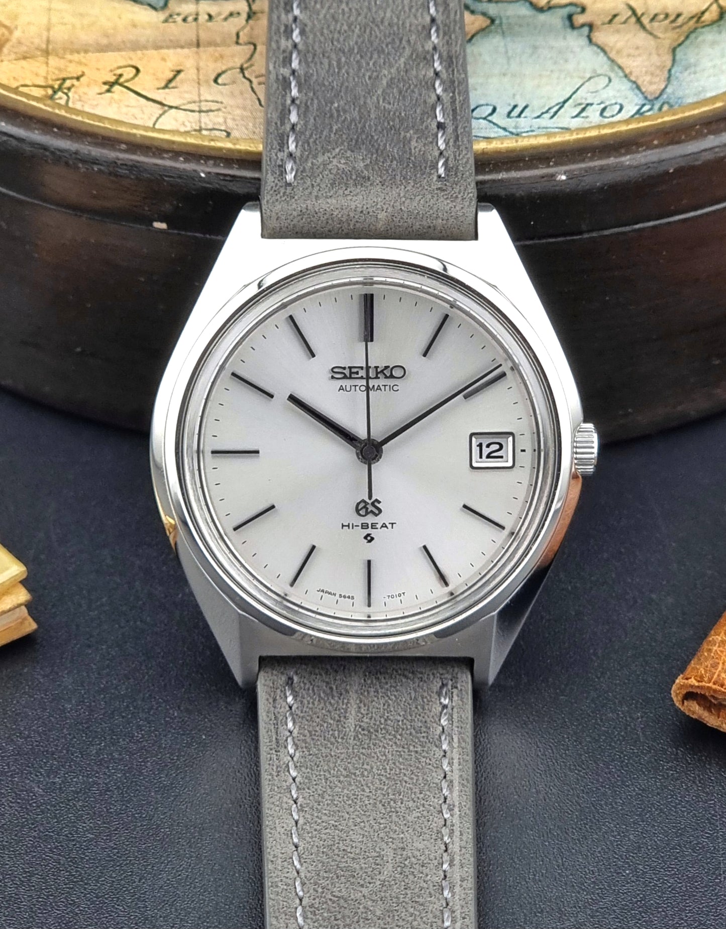 Vintage Grand Seiko watch with gray strap on a dark surface with a world map in the background