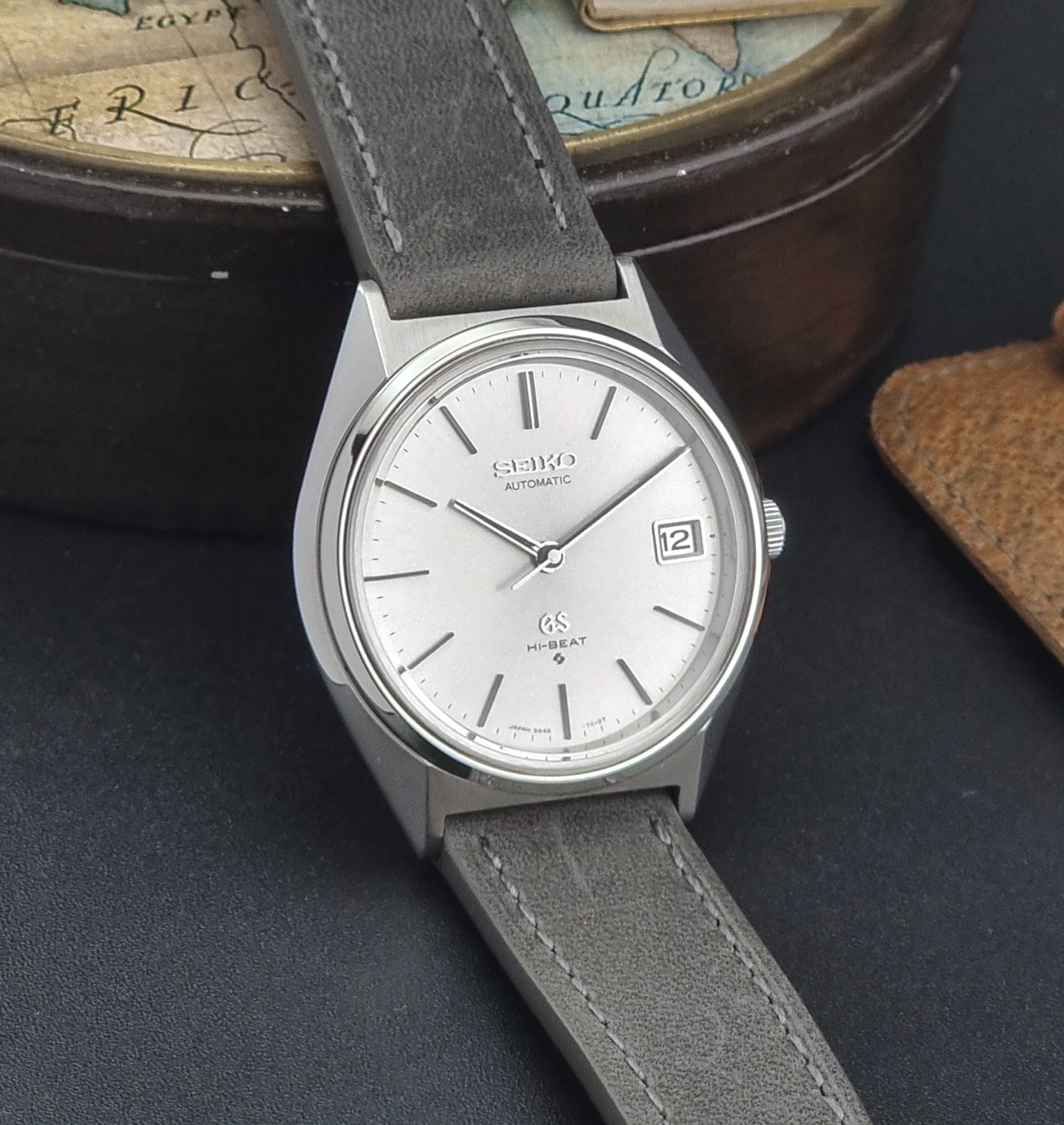 Vintage Grand Seiko watch with gray strap on a dark surface with a world map in the background