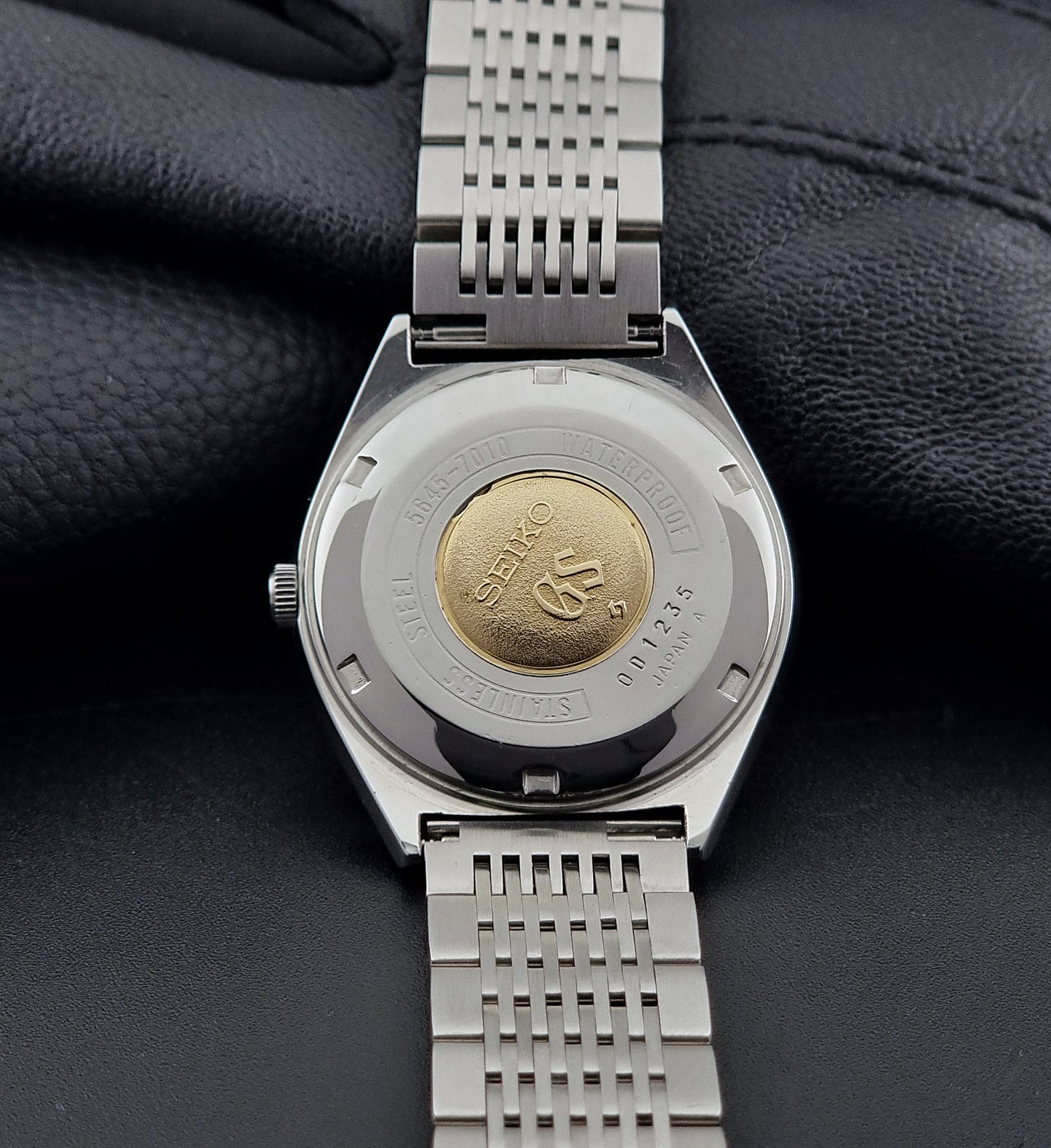Close-up of a Vintage Grand Seiko Wristwatch 5646-7010 case back with a gold emblem on a dark background