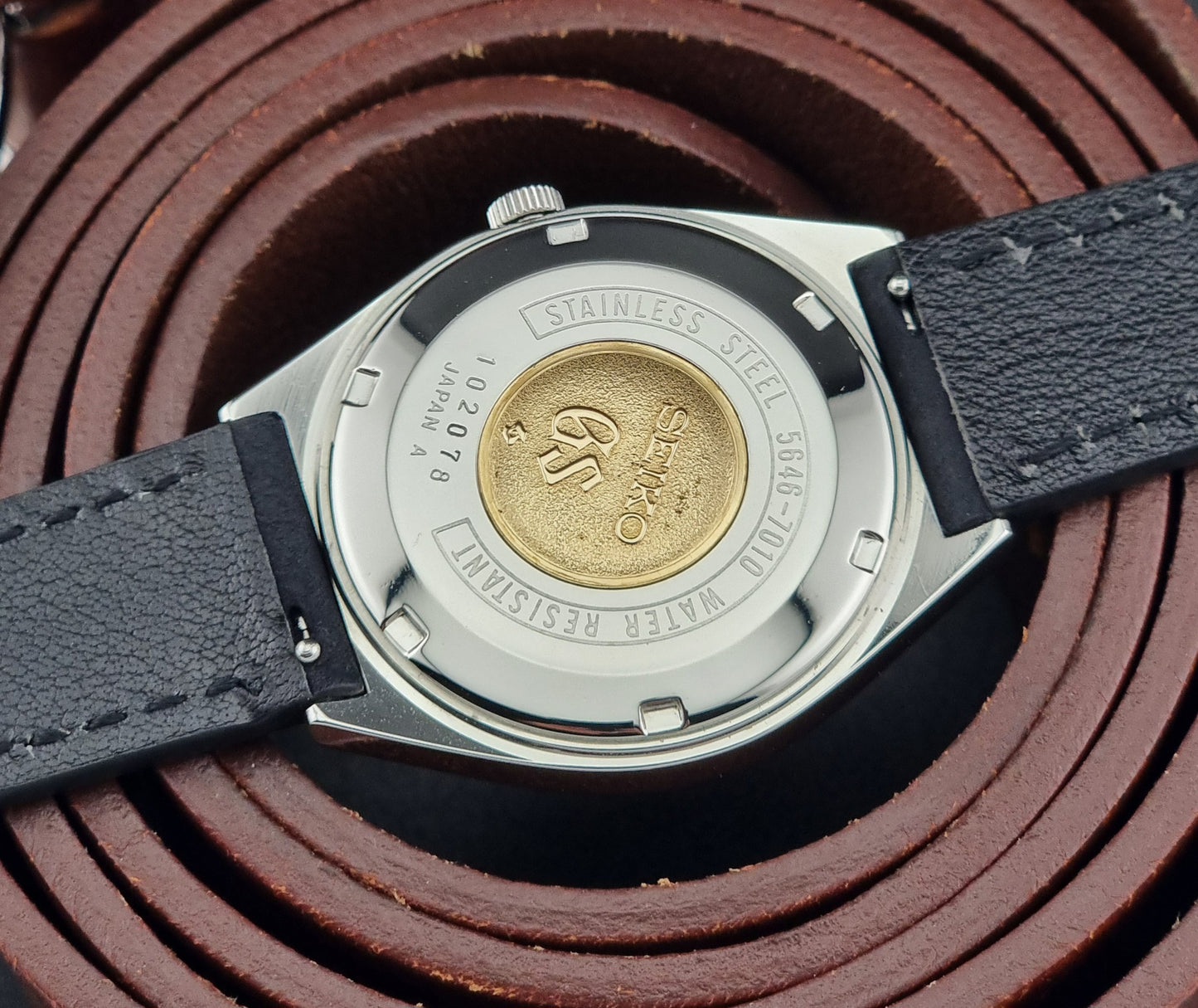 Close-up of a Vintage Grand Seiko watch case with brand logo on a brown leather background