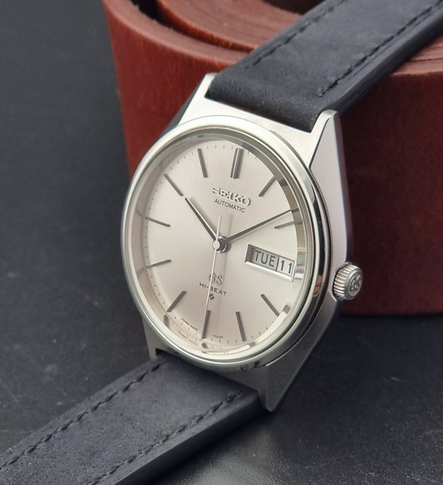 Vintage Grand Seiko watch with a black leather strap on a dark surface
