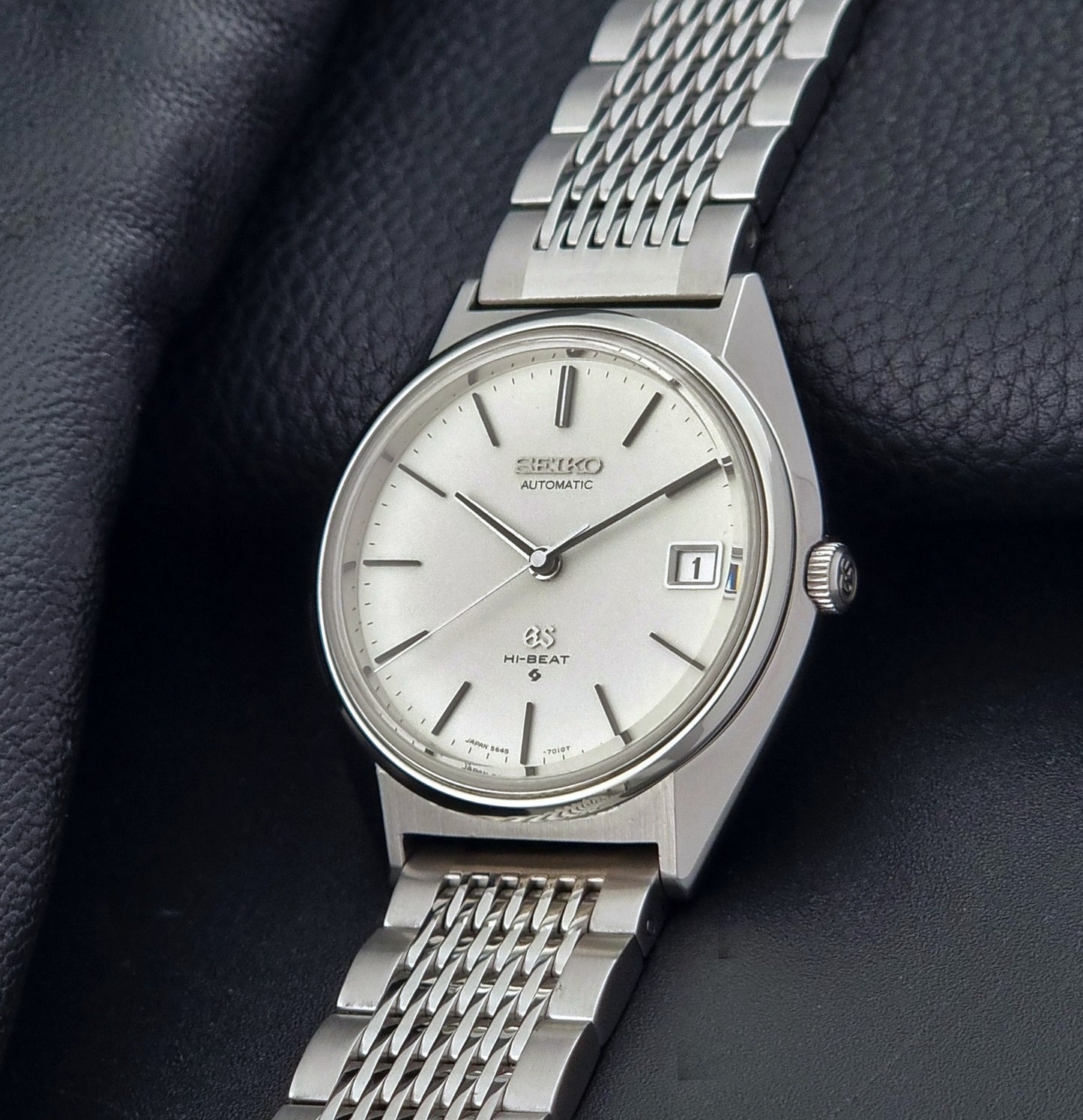 Vintage Grand Seiko Wristwatch 5646-7010 with a white face on a dark textured background crown side view
