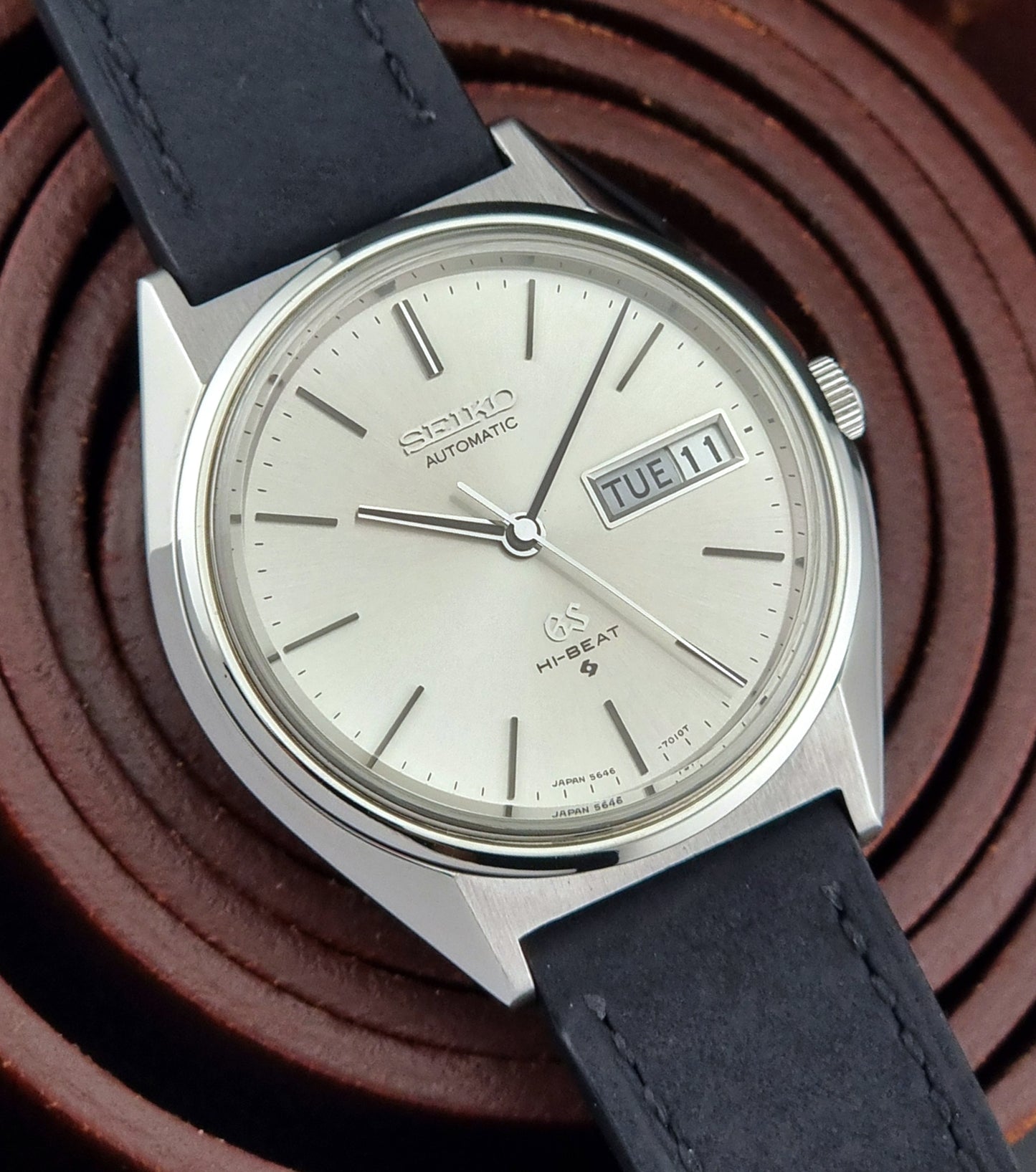 Vintage Grand Seiko watch with black leather strap on a brown textured background
