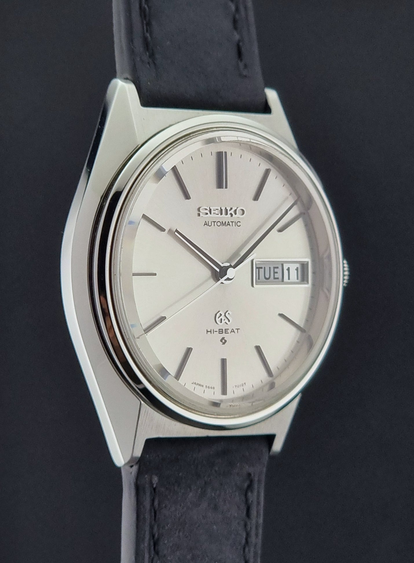 Vintage Grand Seiko watch with a silver dial and black leather strap on a dark background
