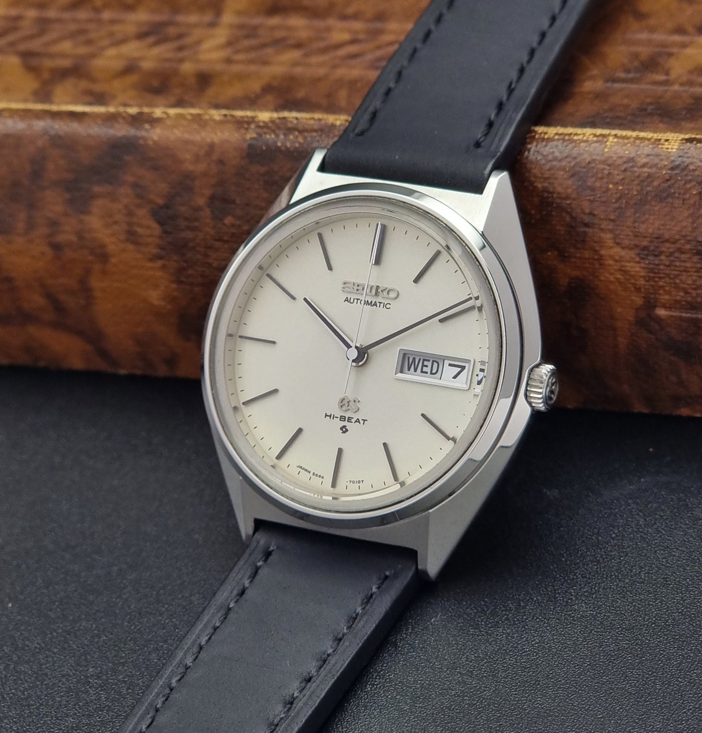 Vintage Grand Seiko 5646-7011 Wristwatch with black leather strap on a wooden surface crown view