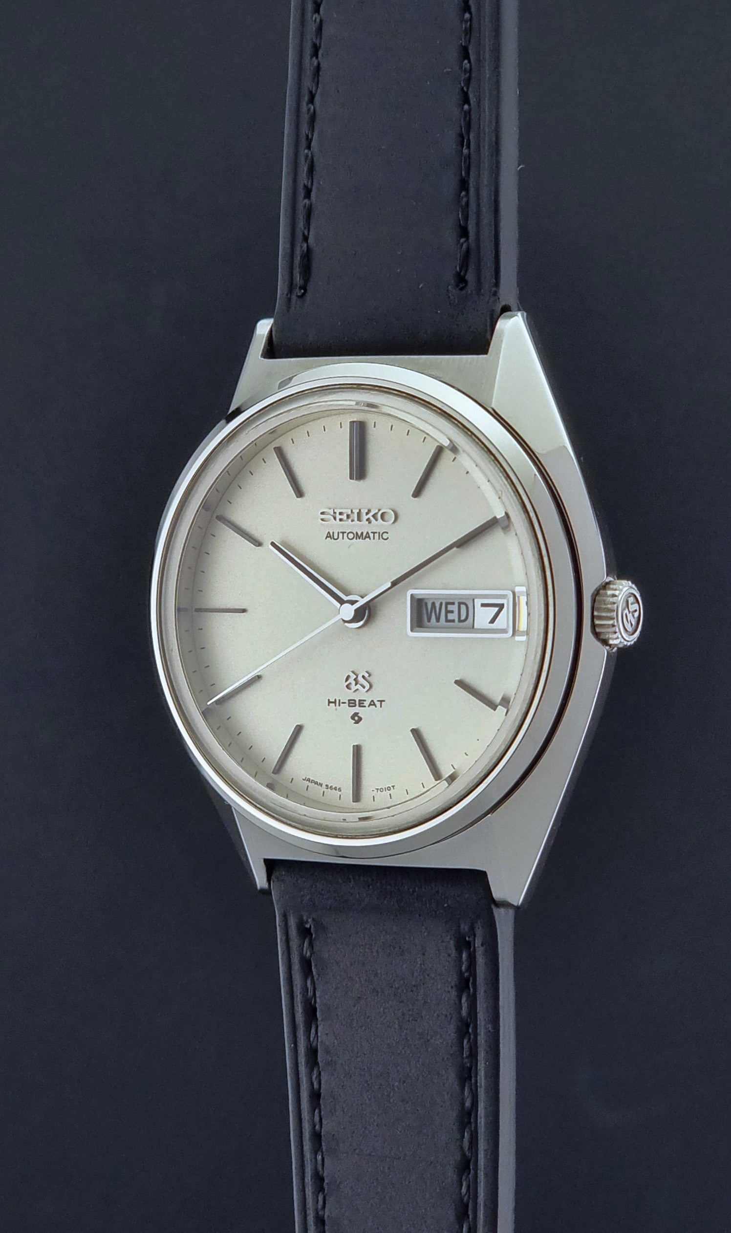 Vintage Grand Seiko 5646-7011 Wristwatch with black leather strap on a wooden surface crown pofile