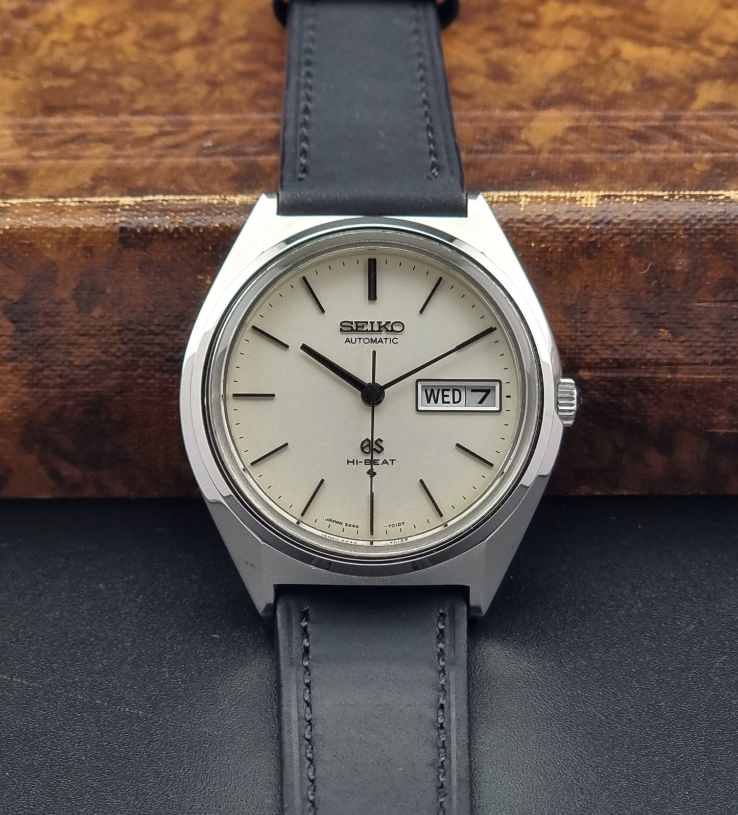 Vintage Grand Seiko 5646-7011 Wristwatch with black leather strap on a wooden surface front view
