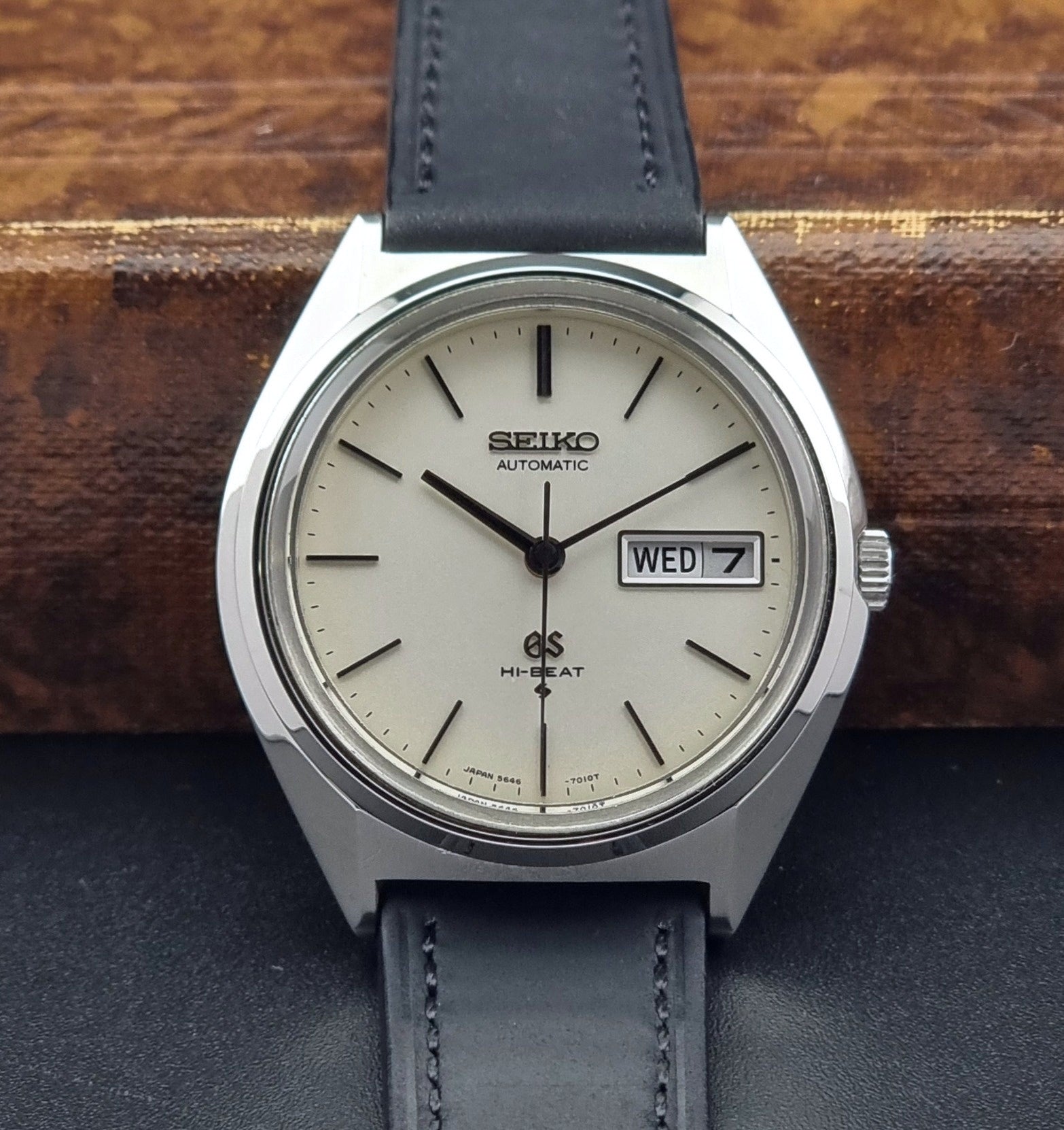 Vintage Grand Seiko 5646-7011 Wristwatch with black leather strap on a wooden surface close up dial