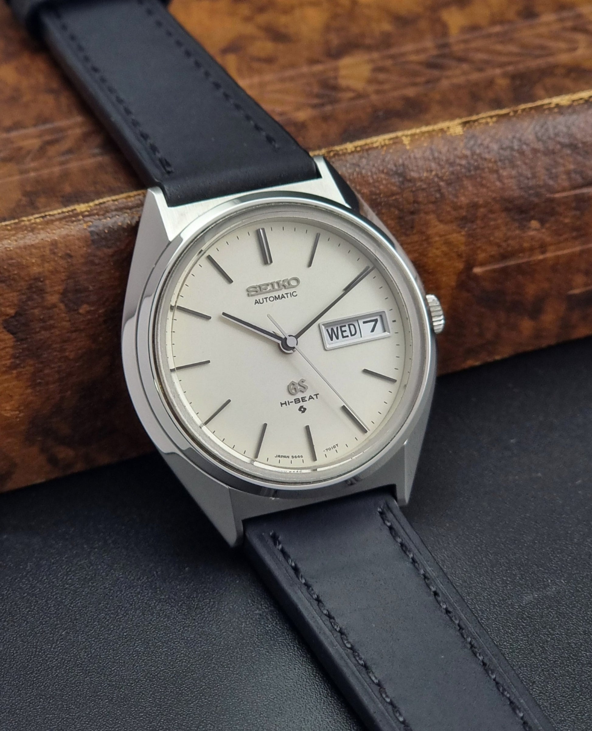 Vintage Grand Seiko 5646-7011 Wristwatch with black leather strap on a wooden surface side view