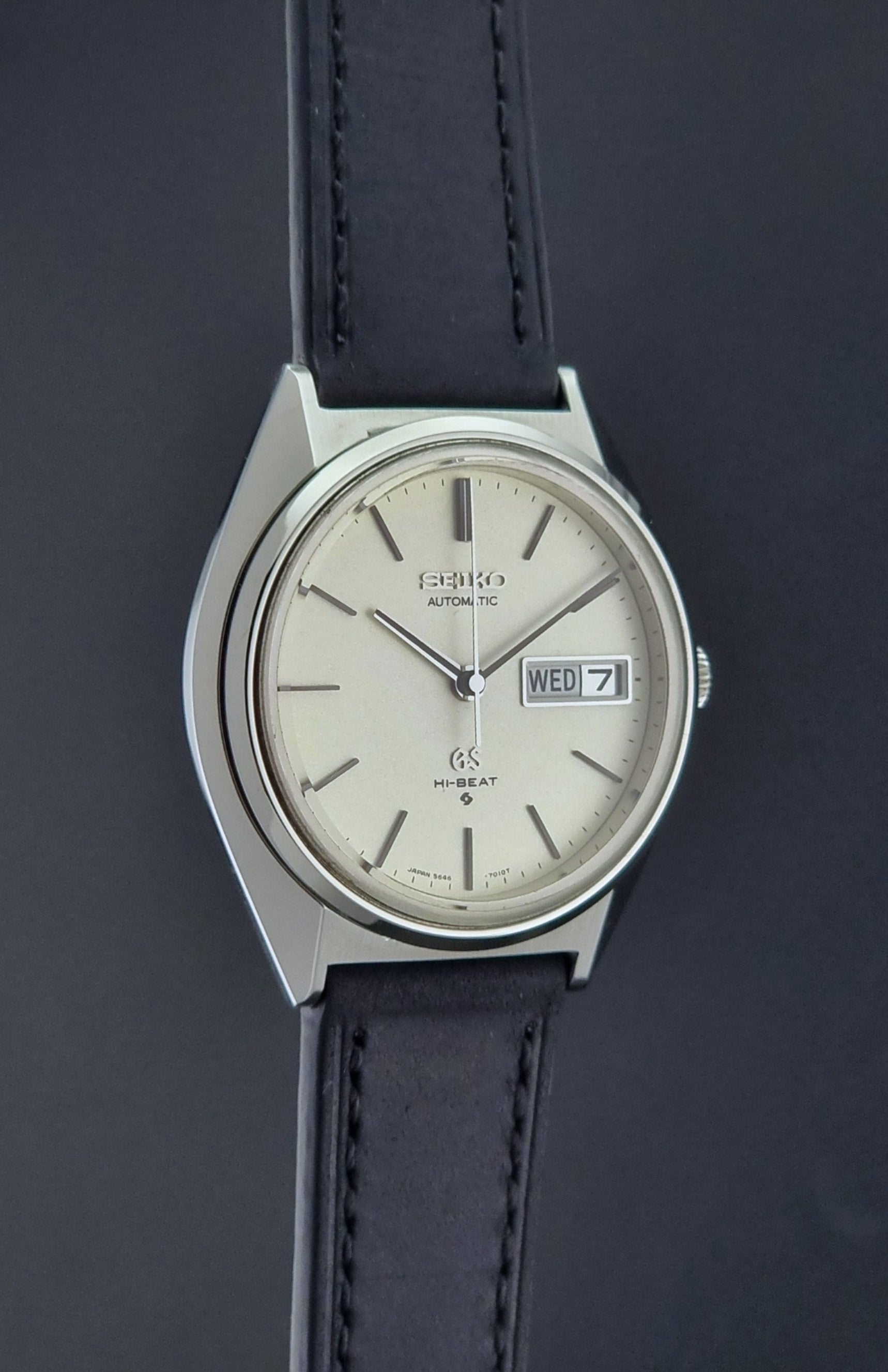 Vintage Grand Seiko 5646-7011 Wristwatch with black leather strap on a wooden surface side profile