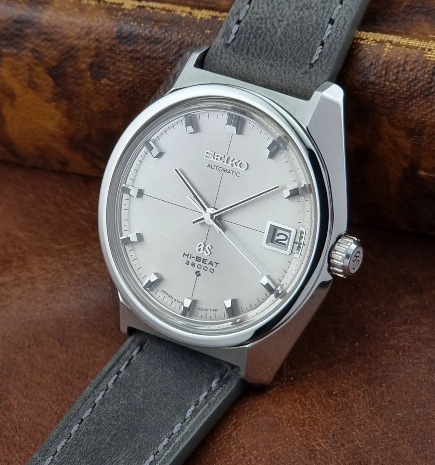 Vintage Grand Seiko watch with gray strap and silver case on a brown leather background